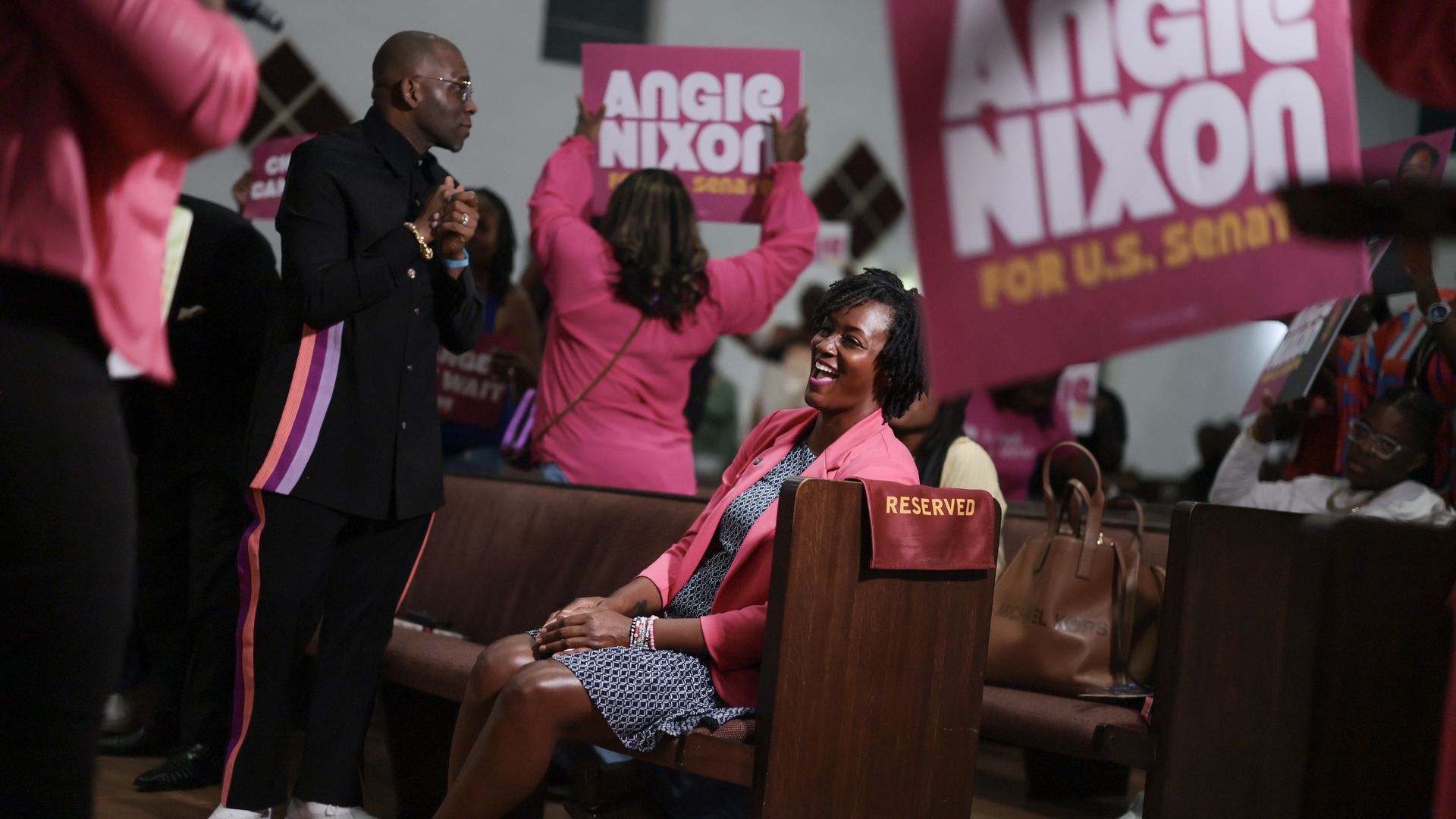 Florida Rep. Angie Nixon sits in a church pew as supporters hold pink “Angie Nixon for U.S. Senate” signs around her.