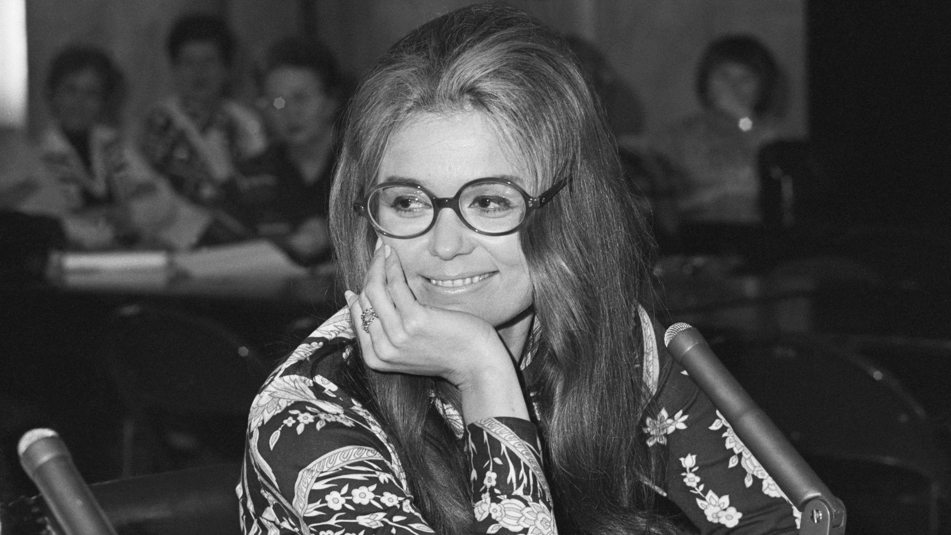 Gloria Steinem sits at a witness table during a 1970 Senate hearing on the Equal Rights Amendment, resting her face on one hand with microphones in front of her.
