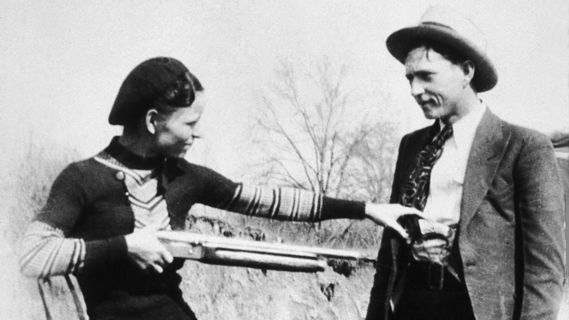A historical photo of Bonnie Parker pointing a shotgun at Clyde Barrow