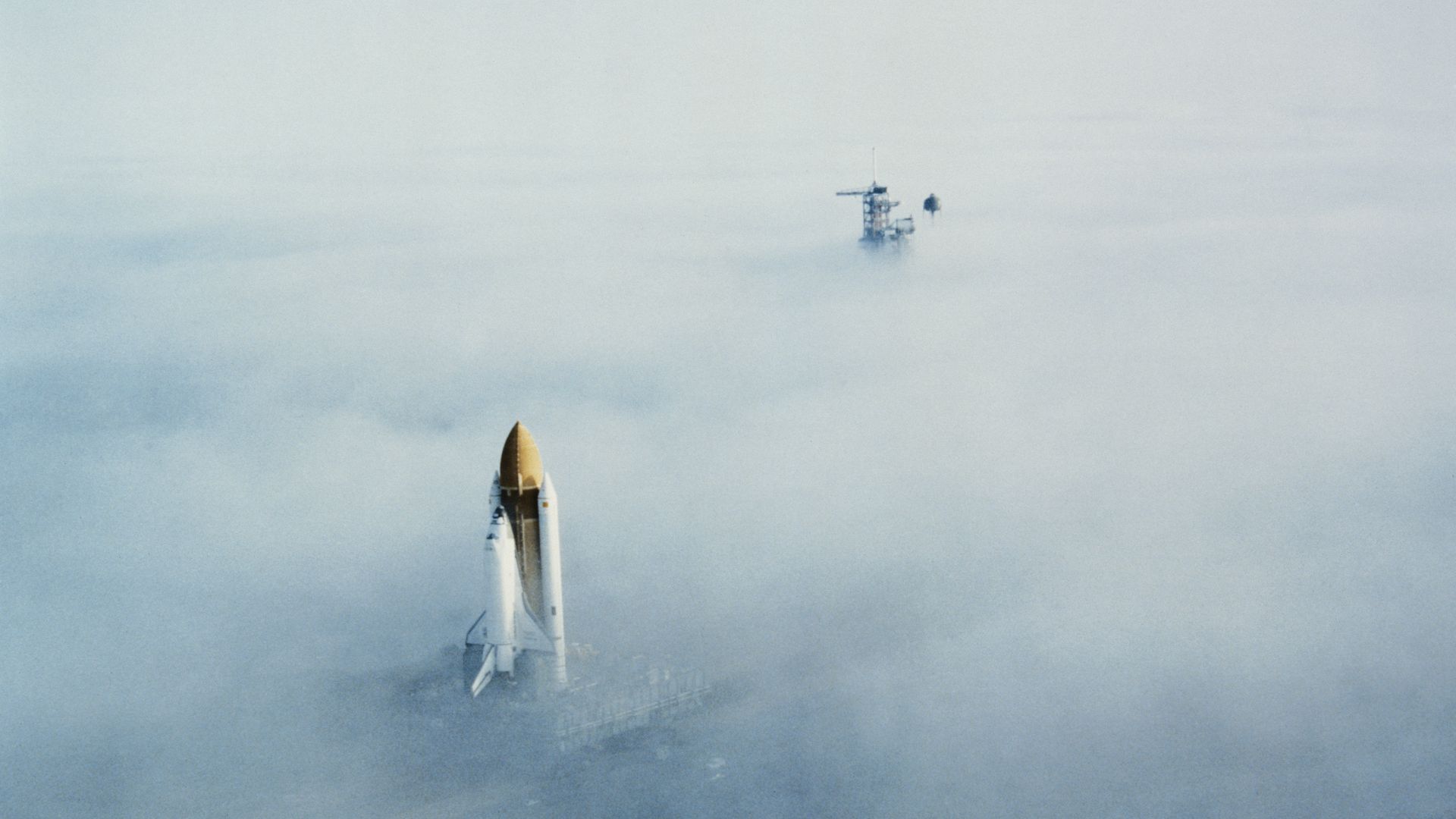 The Challenger shuttle pokes through clouds as it is moved toward its launch pad