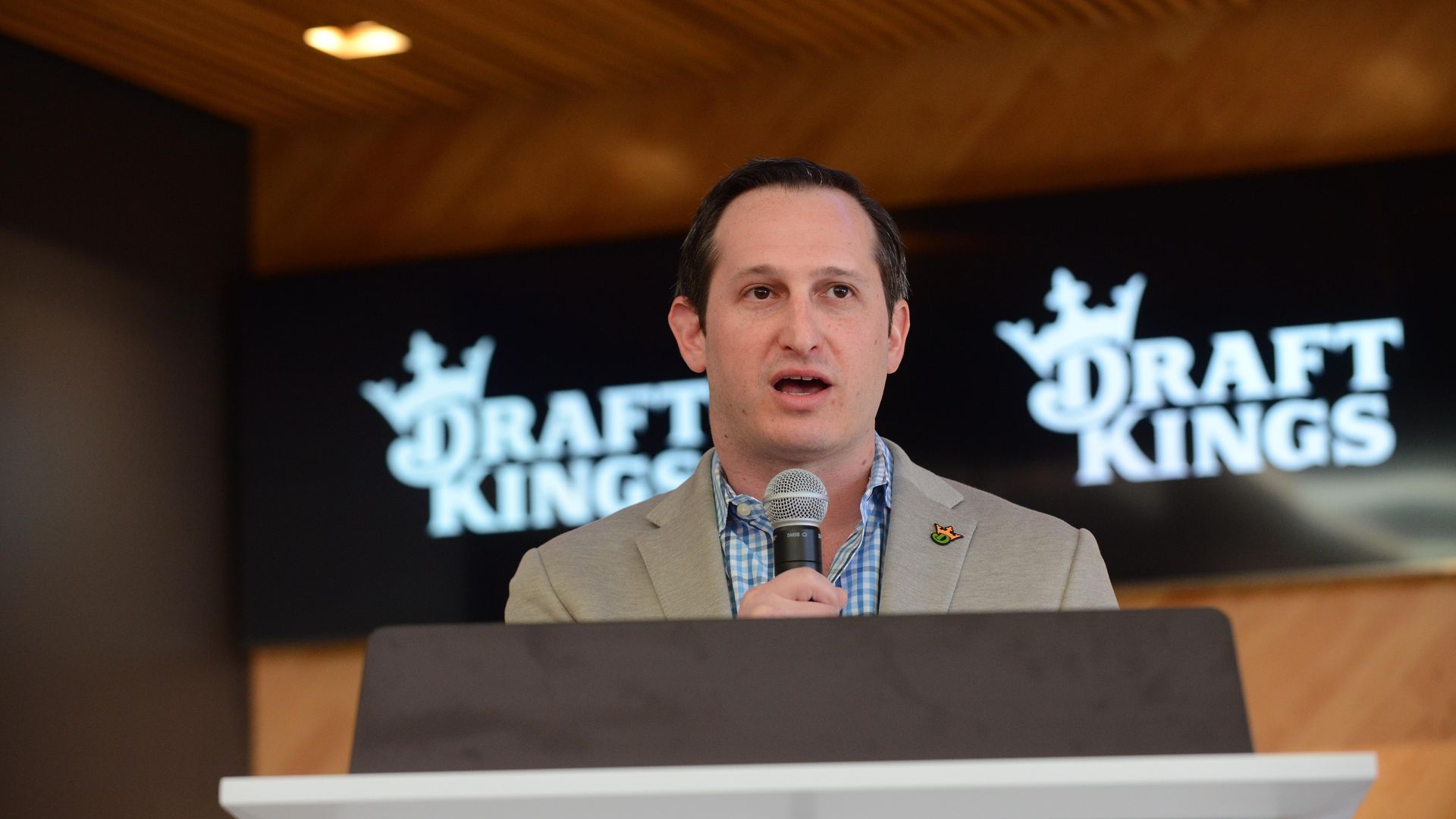 A person in a gray suit speaks behind a lectern with a microphone