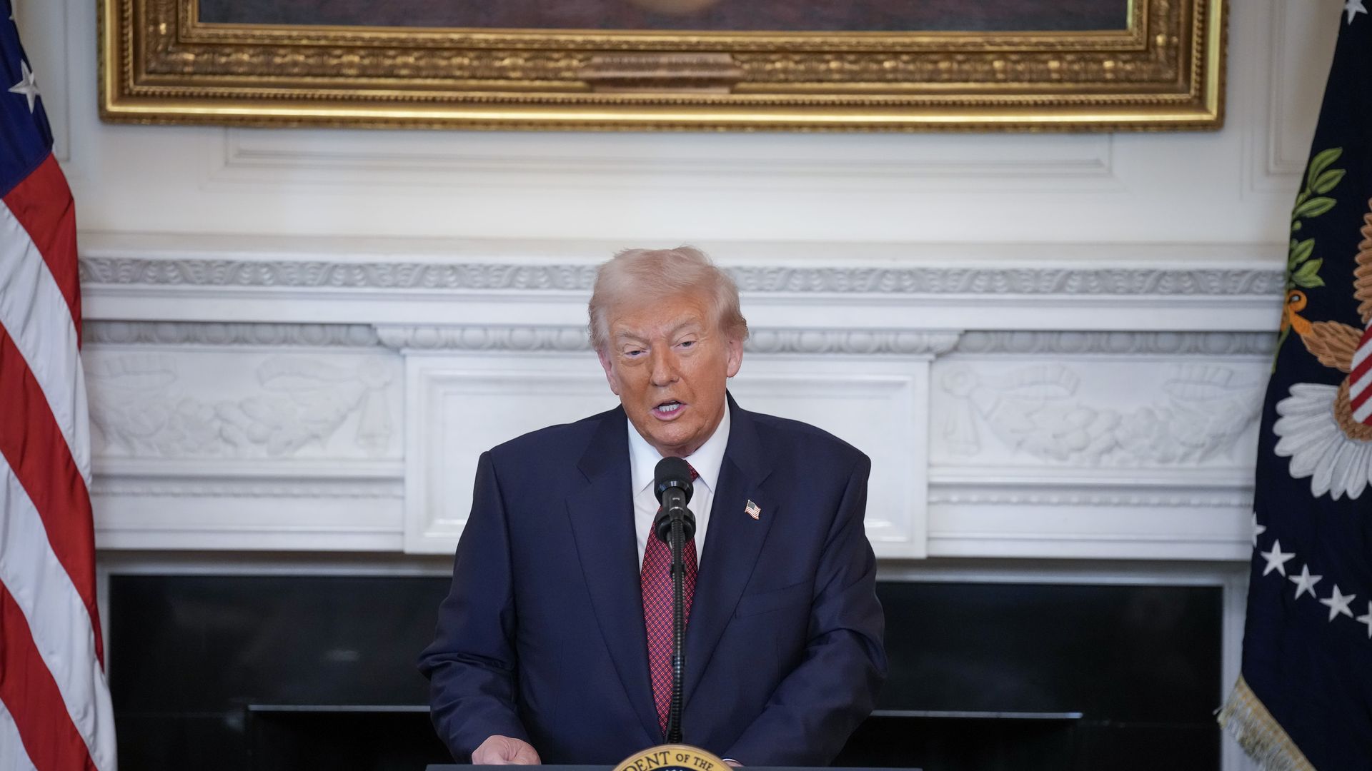 Trump wearing a navy suit with an American flag pin, white shirt and red tie