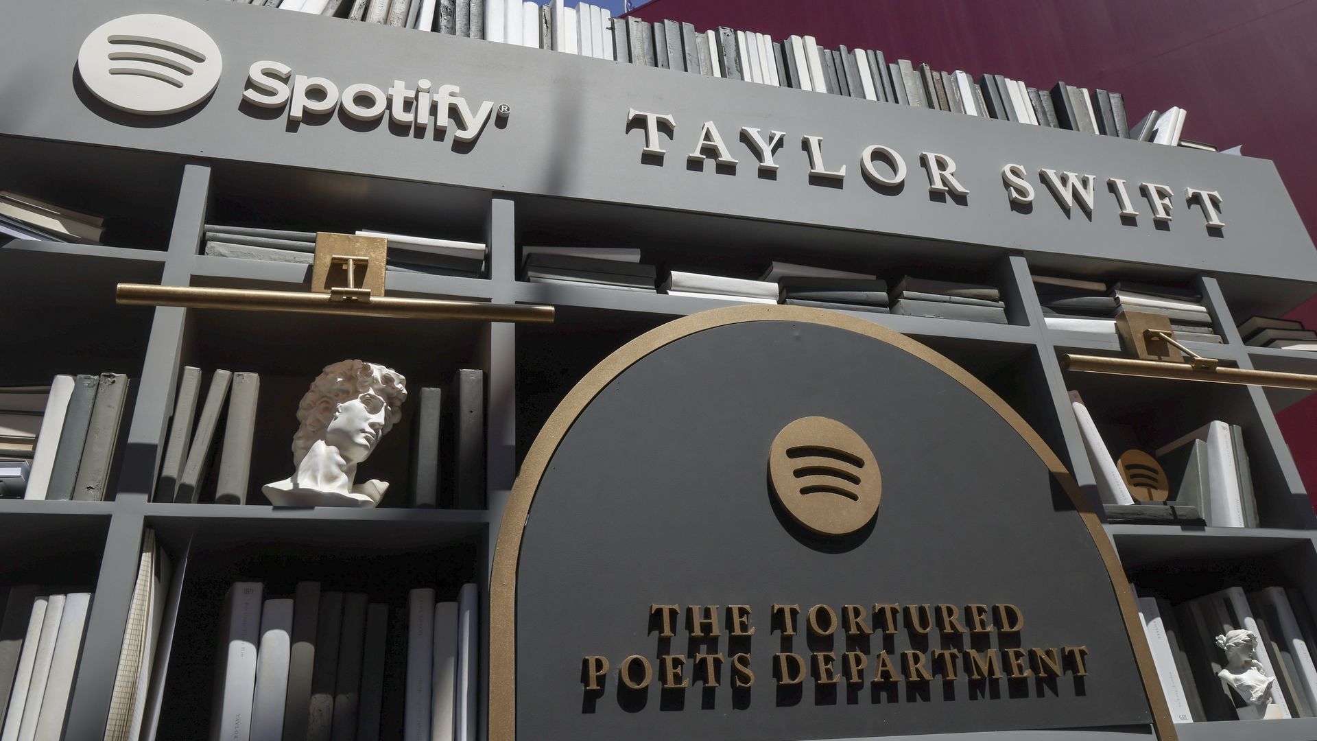 A bookshelf with gray and white books and signs that say "Spotify Taylor Swift" and "The Tortured Poets Department."