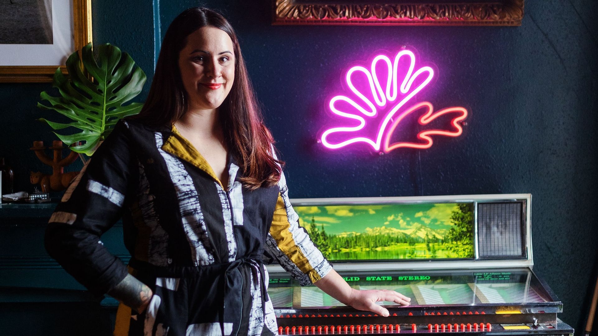A portrait of Bronwen Wyatt standing next to a jukebox.