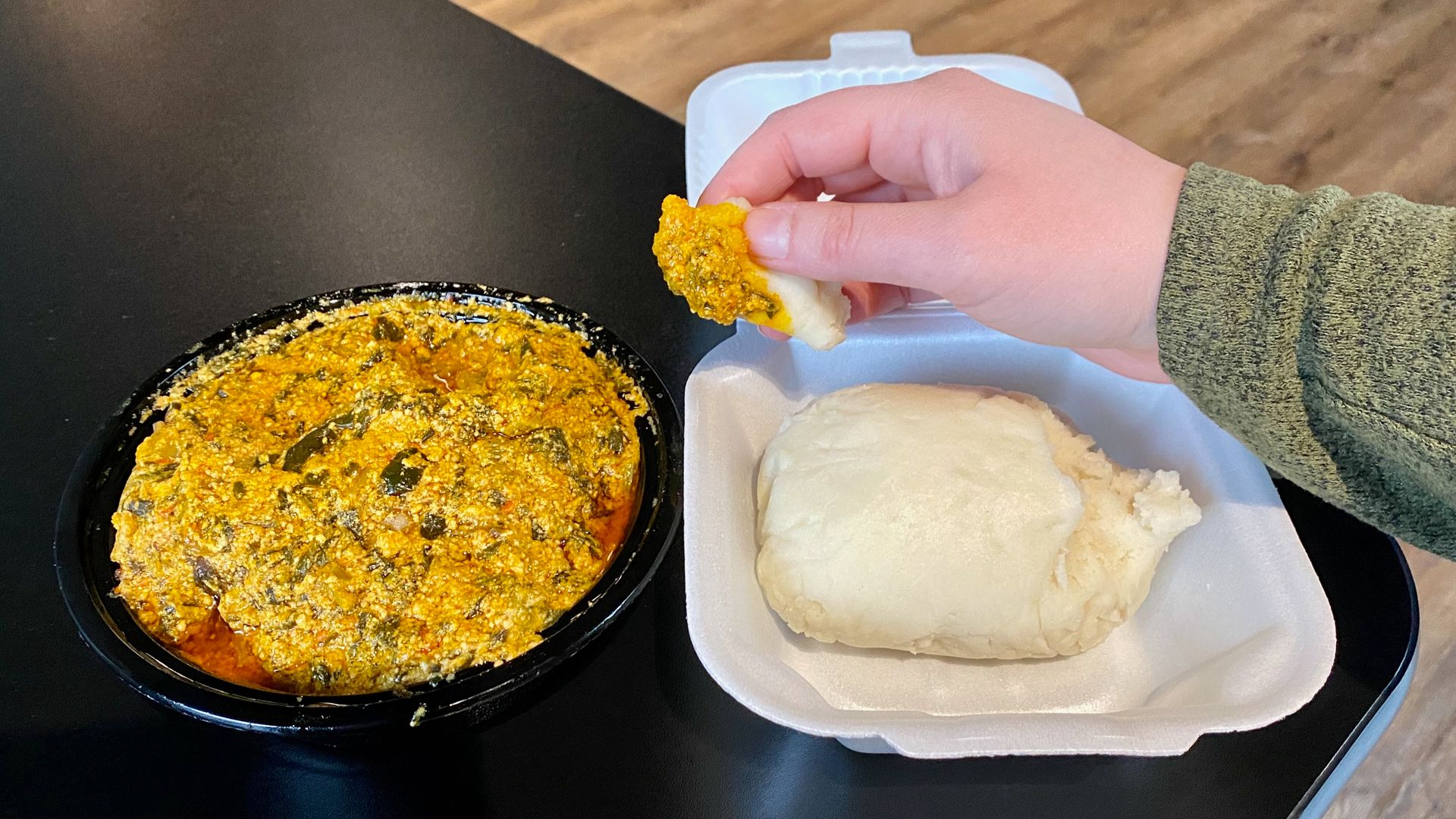 Alissa's hand holding a small piece of fufu dough after scooping Egusi soup onto it