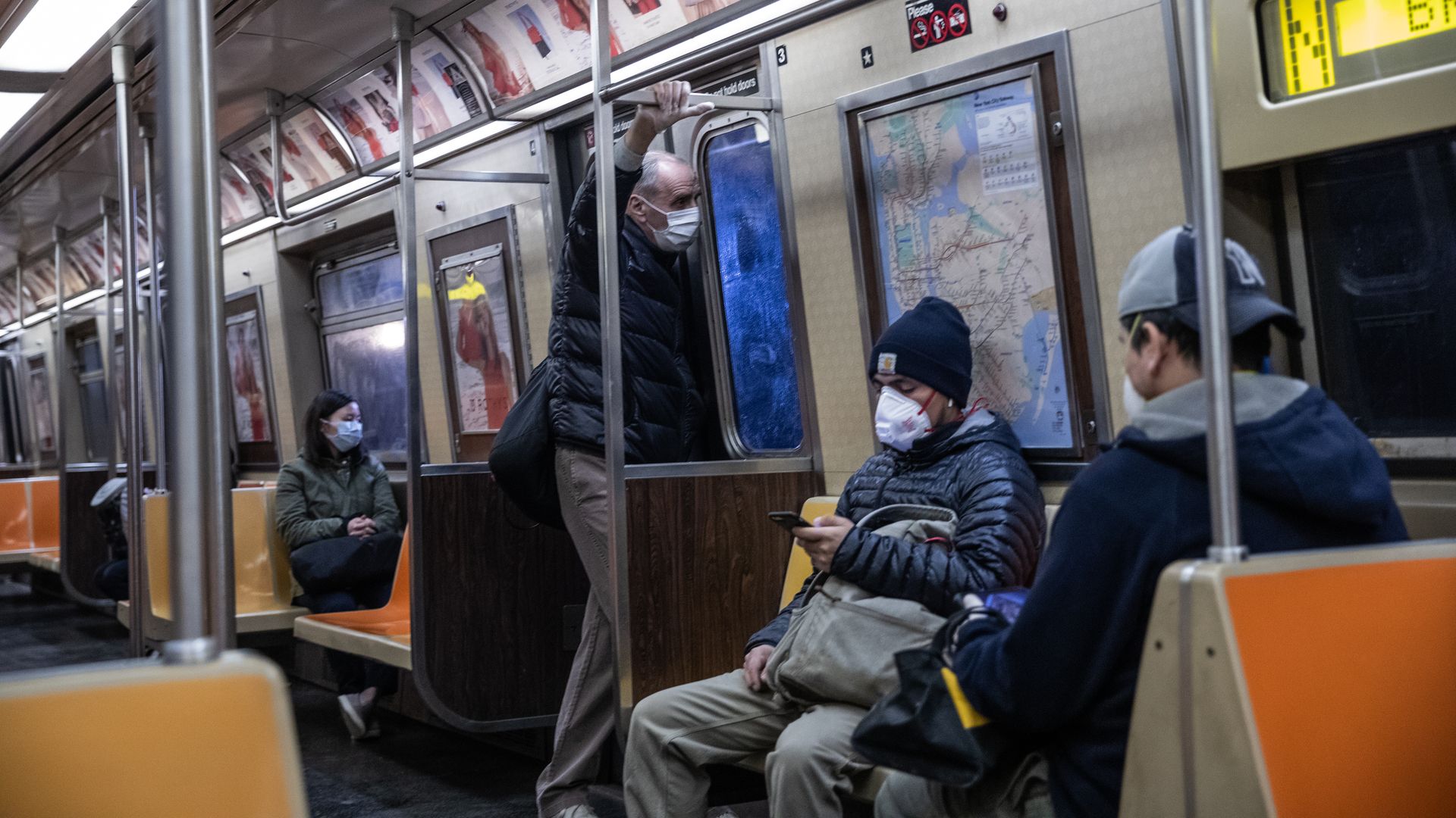 In this image, several people sit on a subway while wearing masks