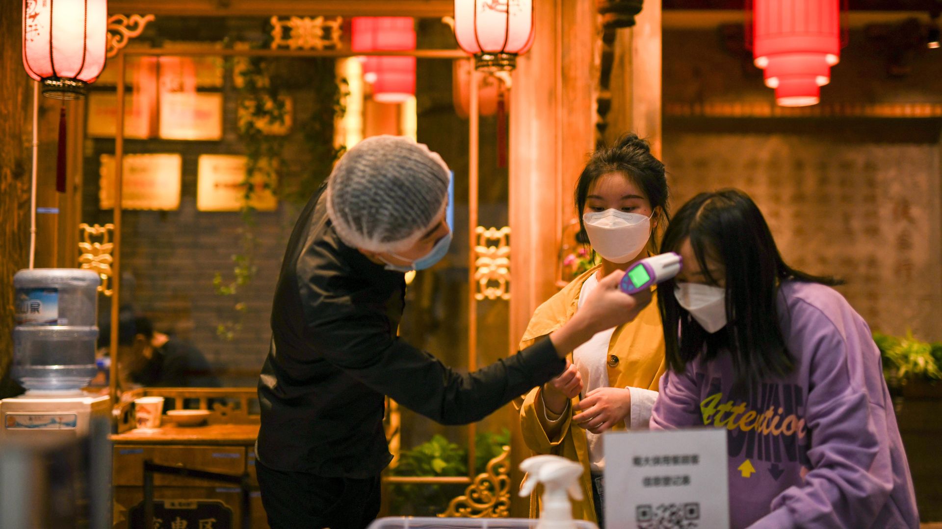 A restaurant employee checks the temperature of two customers wearing face masks.