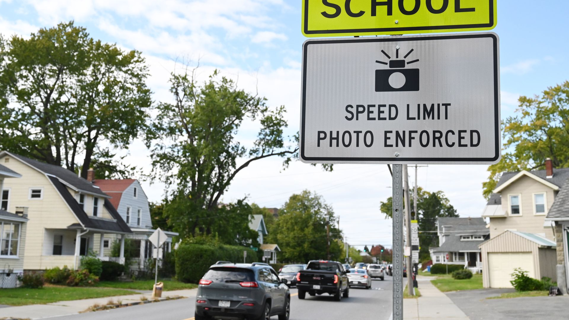A sign reading "Speed Limit Photo Enforced" next to a city street with cars backed up