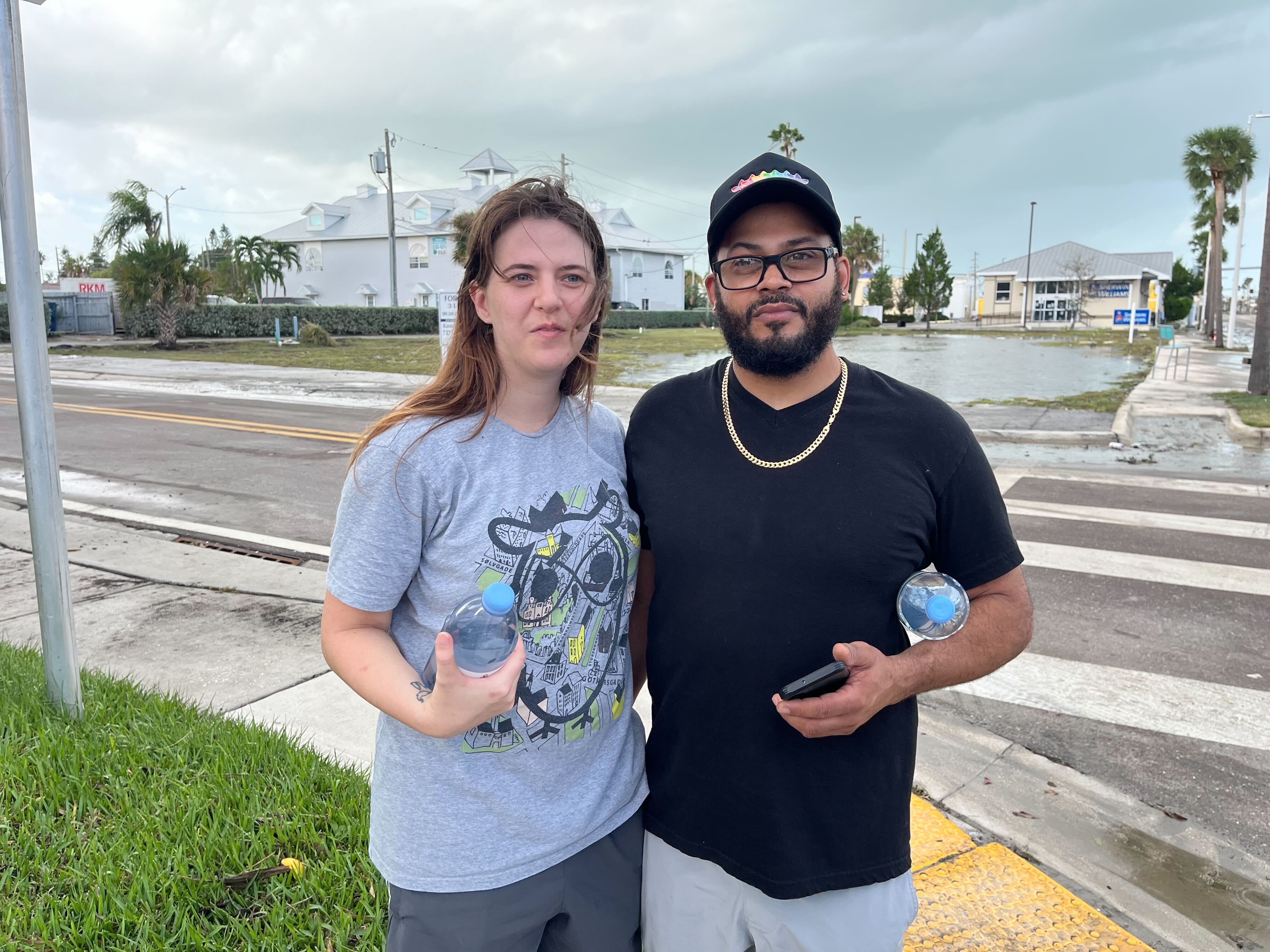 A couple standing near a roadway holding water bottles.
