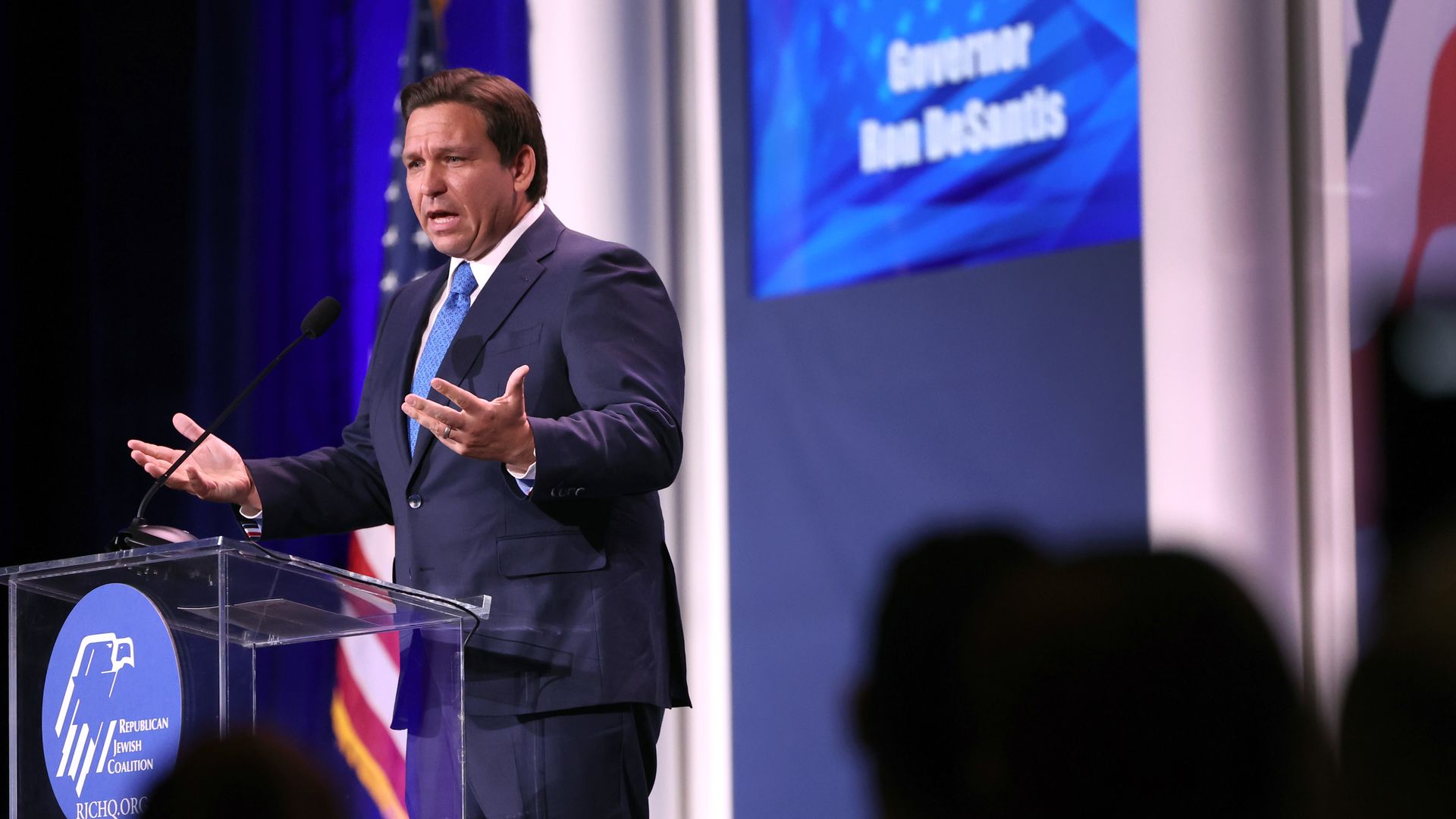 Photo of Ron DeSantis gesturing with his hands while he speaks from a podium