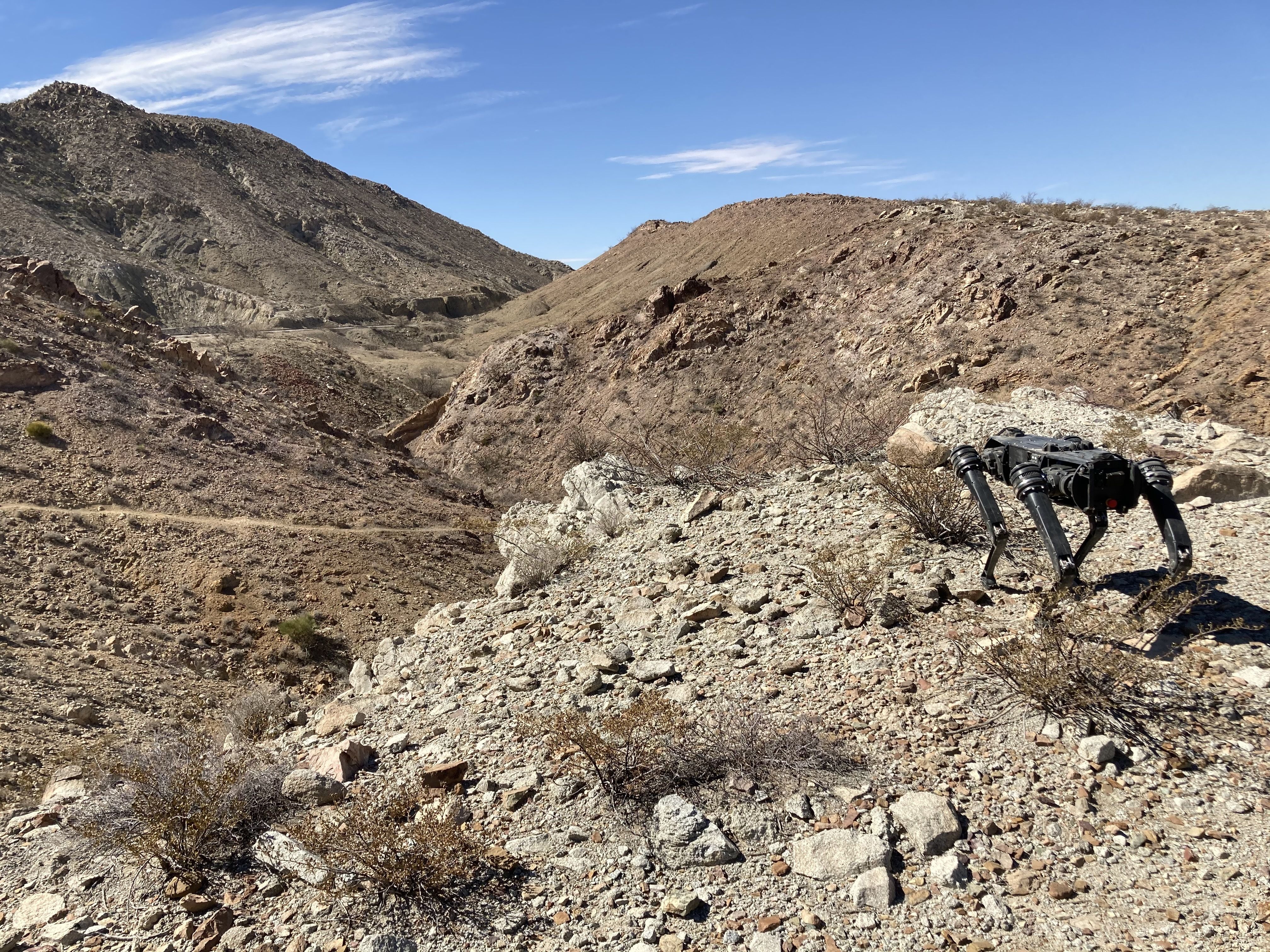 A robot dog overlooks a desert terrain along the U.S.-Mexico border with mountains in the background.