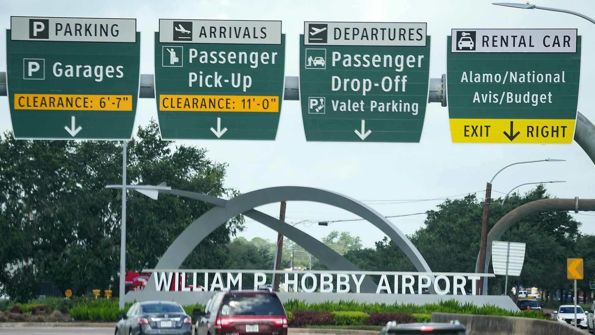 Highway signs at William P. Hobby Airport directing to parking garages, passenger pick-up, passenger drop-off with valet, and rental car exit for Alamo, National, Avis, Budget.