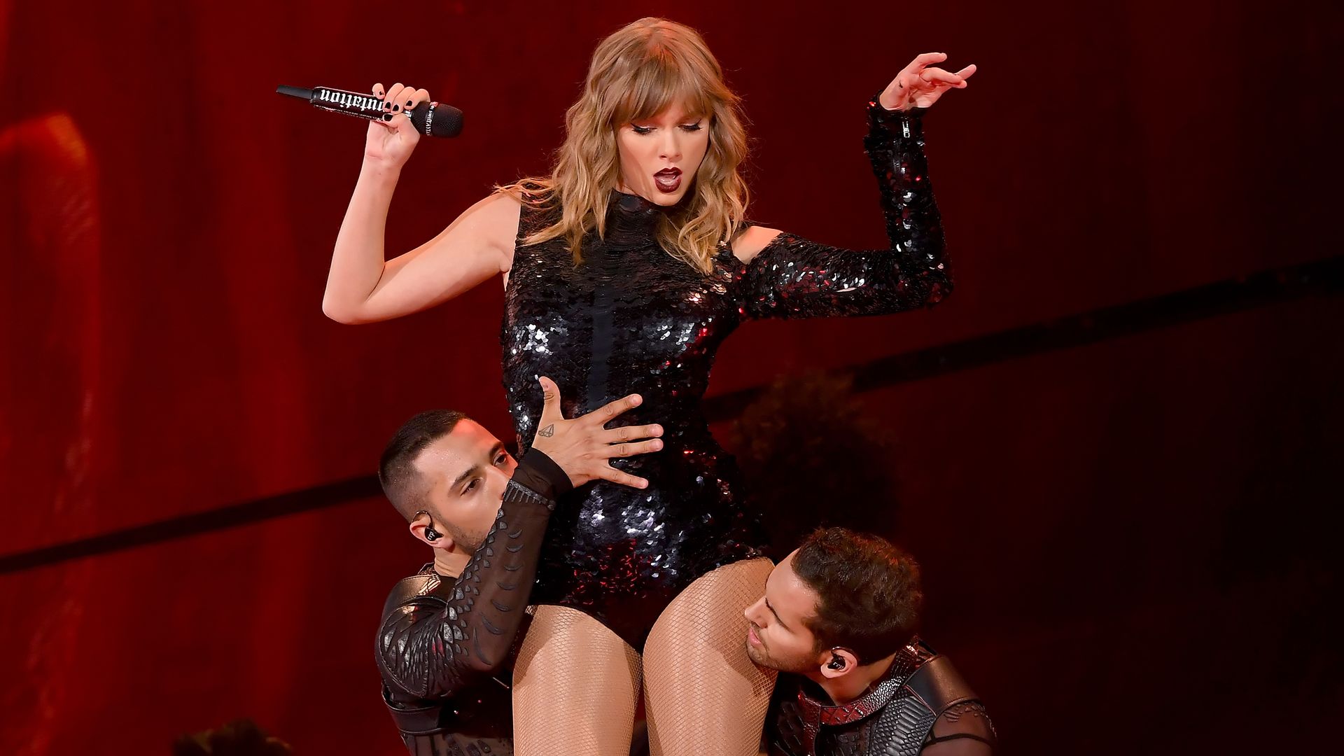 Taylor Swift with two male dancers on stage.