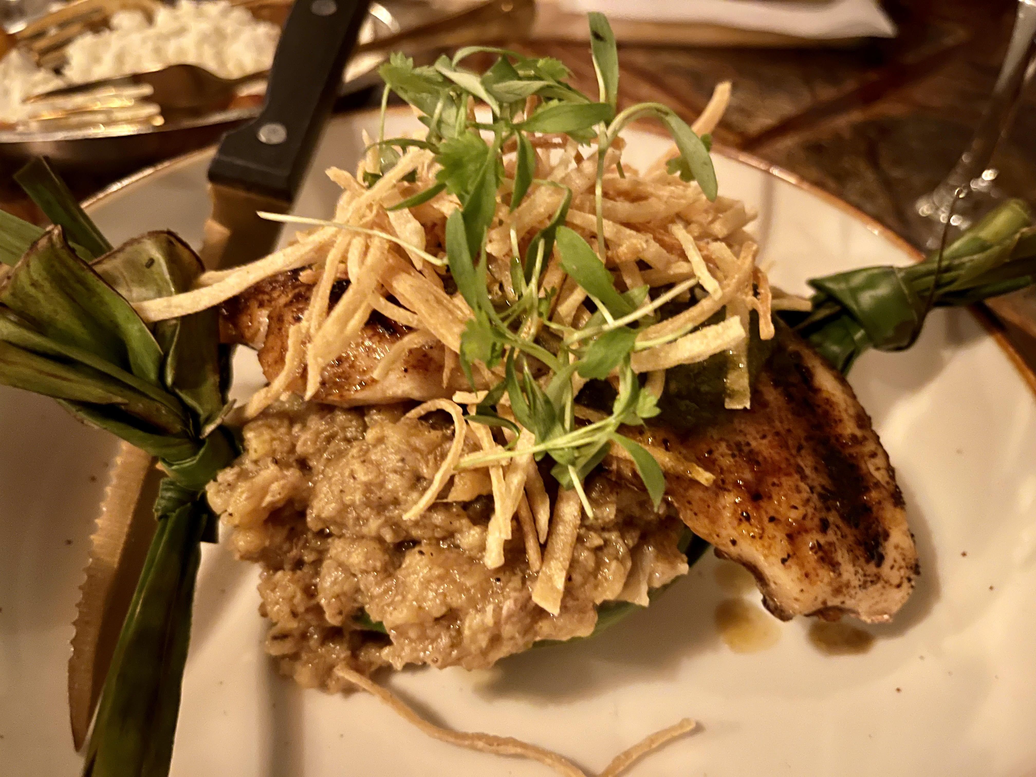 A fish filet on top of mashed plantains topped with crispy slices of potato. 
