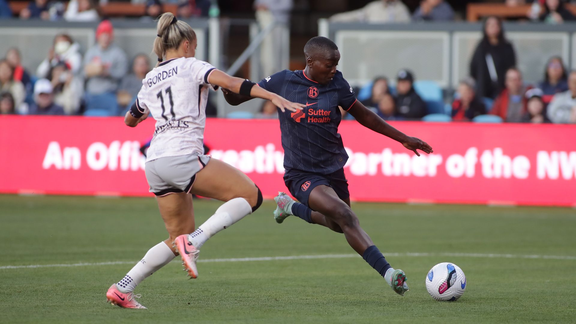 Photo of a Bay FC player drawing her leg back to kick a soccer ball as an Angel City player defends