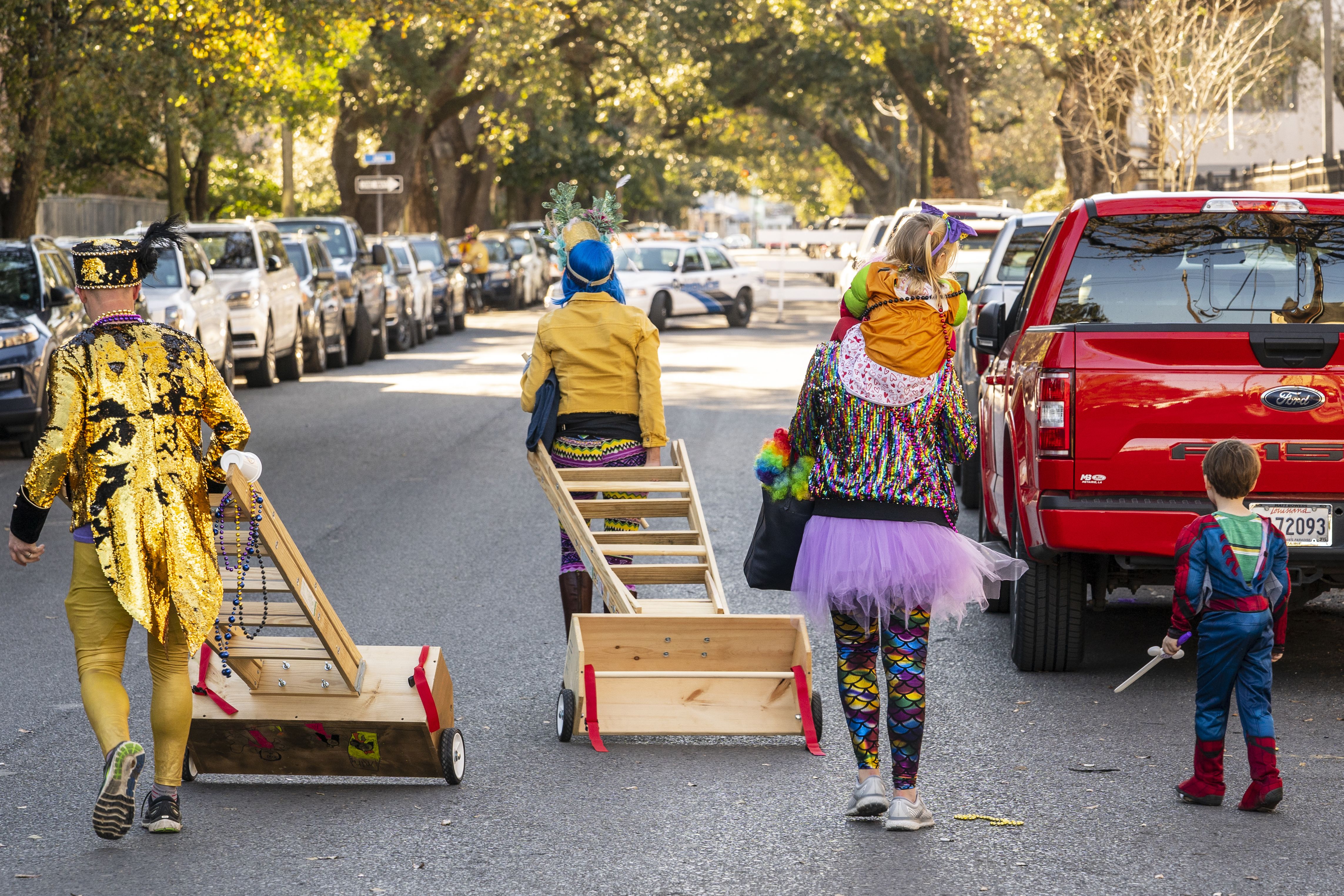 Photo shows costumed people walking away from a parade carrying ladders