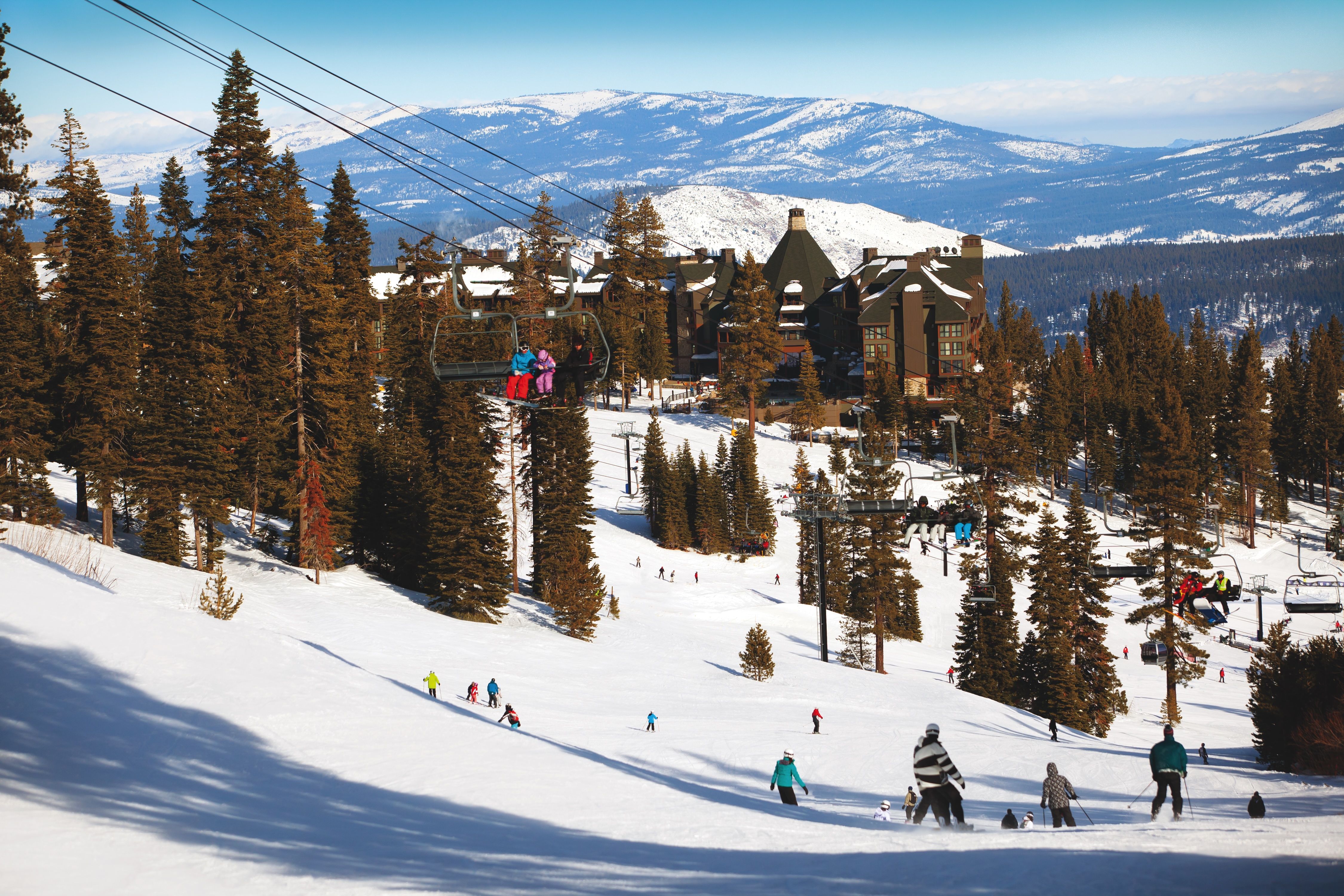 A photo of people on a ski lift with a resort covered in snow in the background.