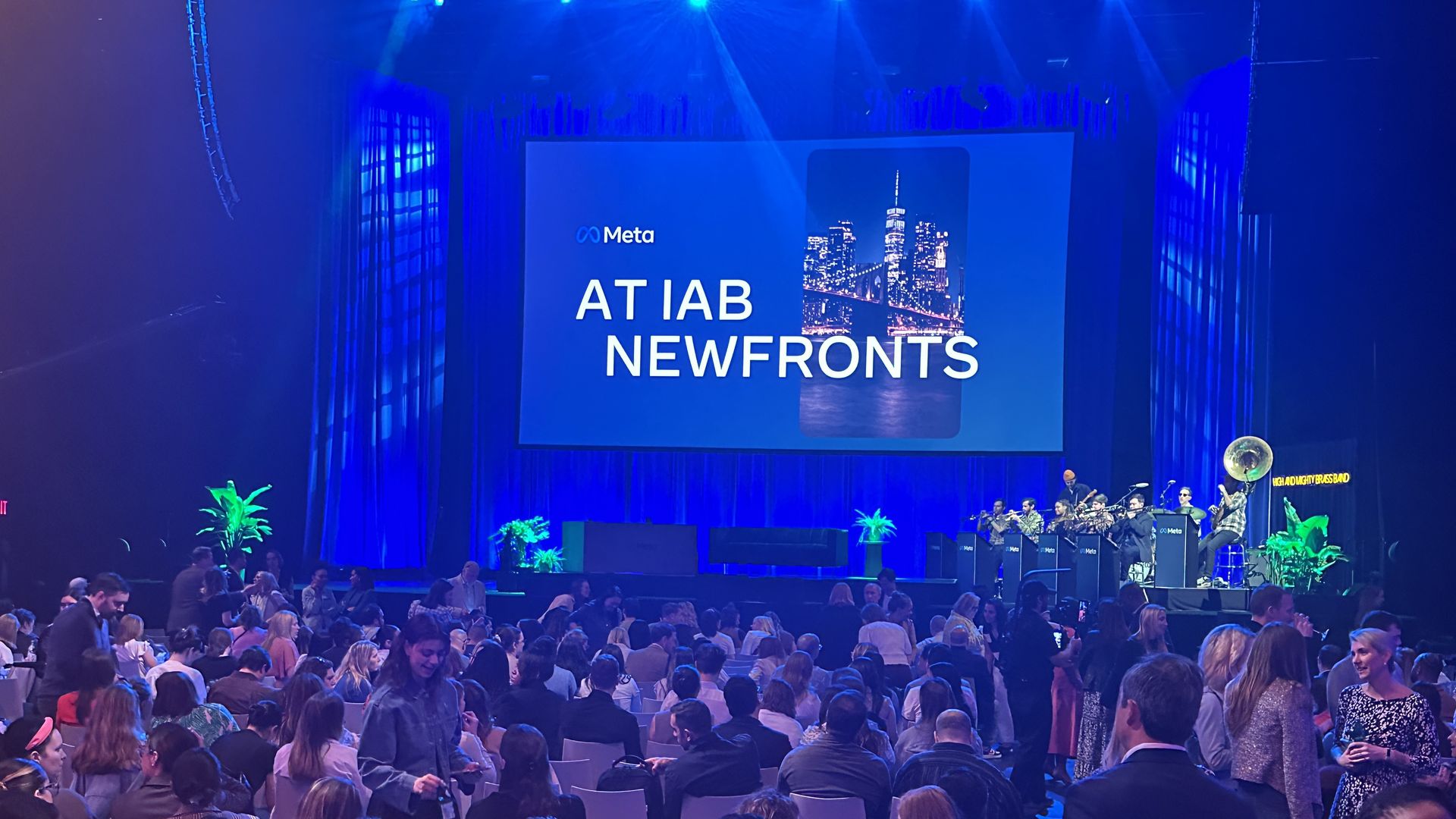 Crowded room of people standing and sitting with a screen in the back that says Meta at IAB NewFronts. There's a band onstage