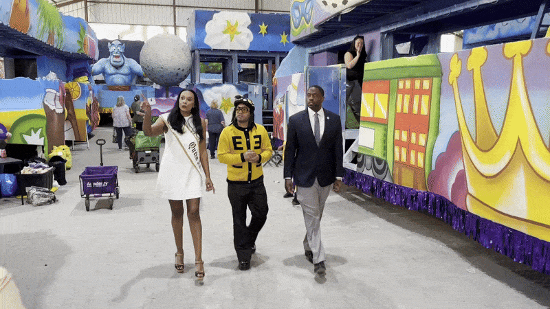 Three people walk along a Mardi Gras float in a den.