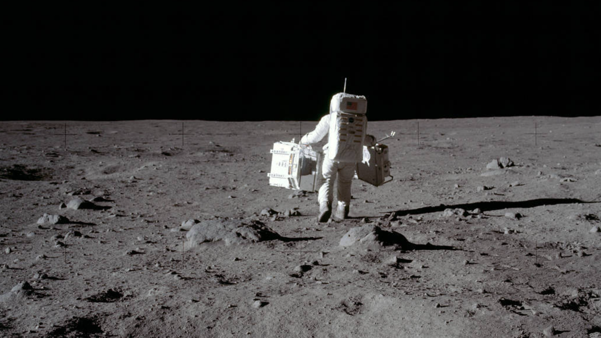 An astronaut is shown on the surface of the moon, facing away from the camera.