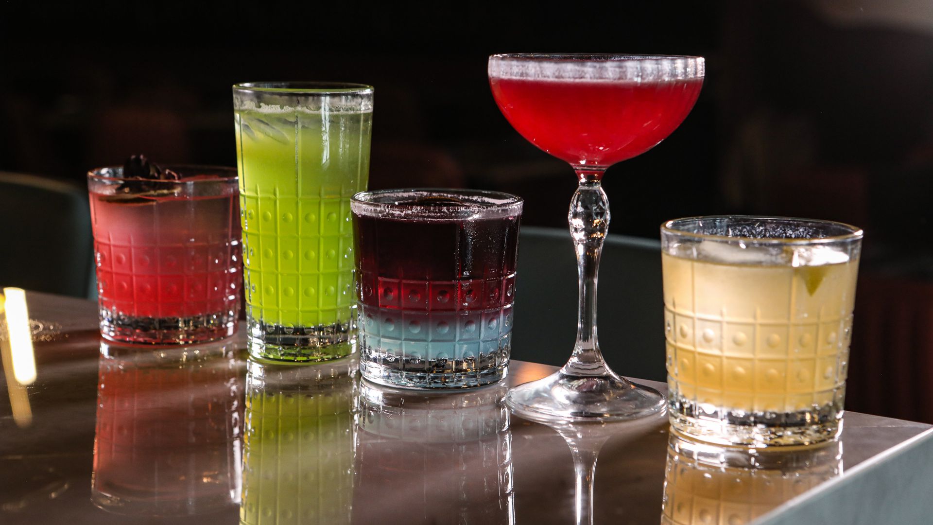 Five brightly colored cocktails in various shaped cocktail glasses.