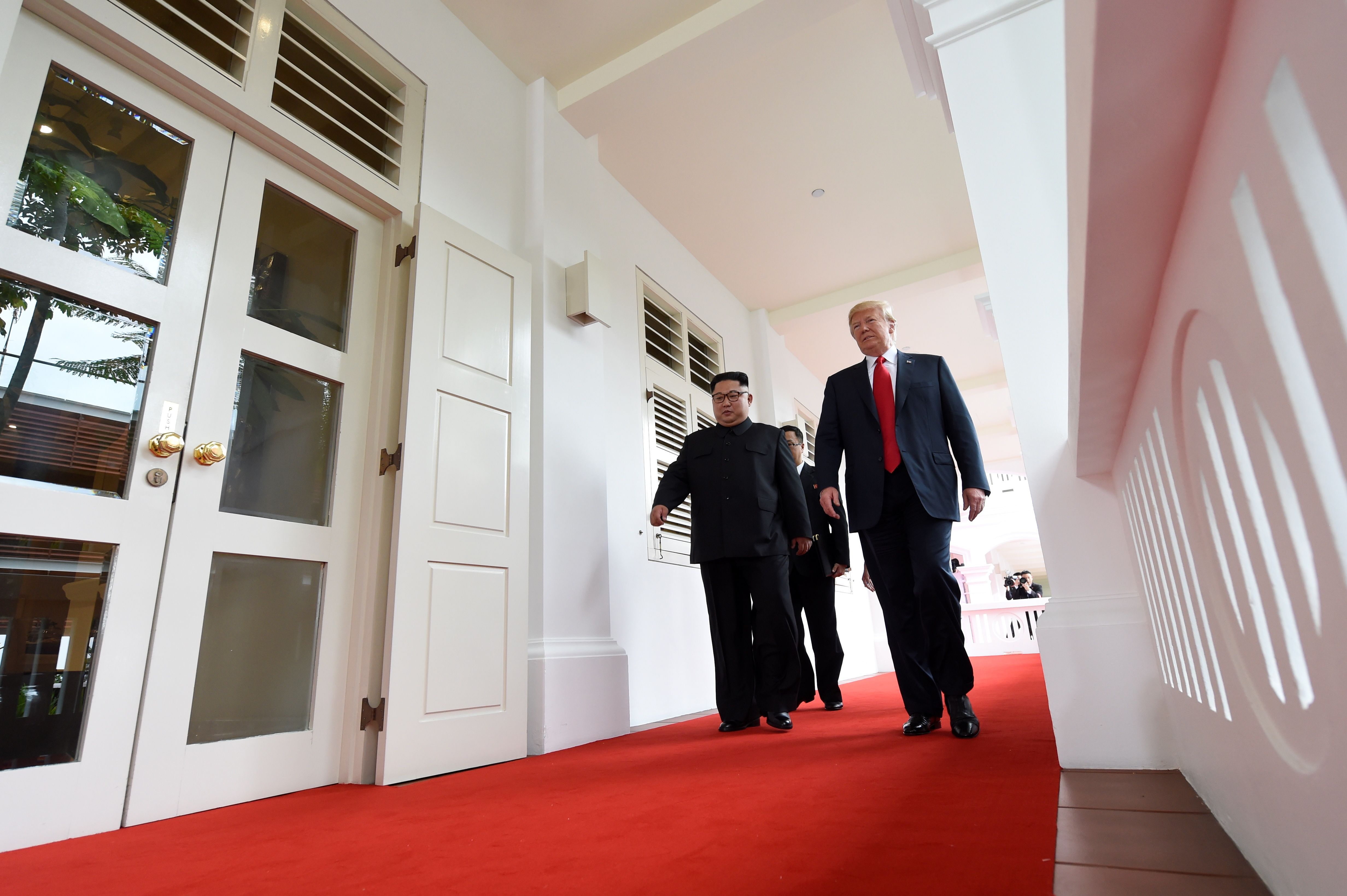 Trump adn Kim walk down a colonnade smiling 