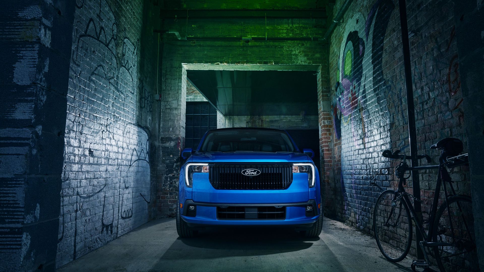 Blue Ford Maverick Lobo pickup truck parked in a narrow, graffiti-covered brick alley with green and blue lighting, a bicycle leans against the right wall.