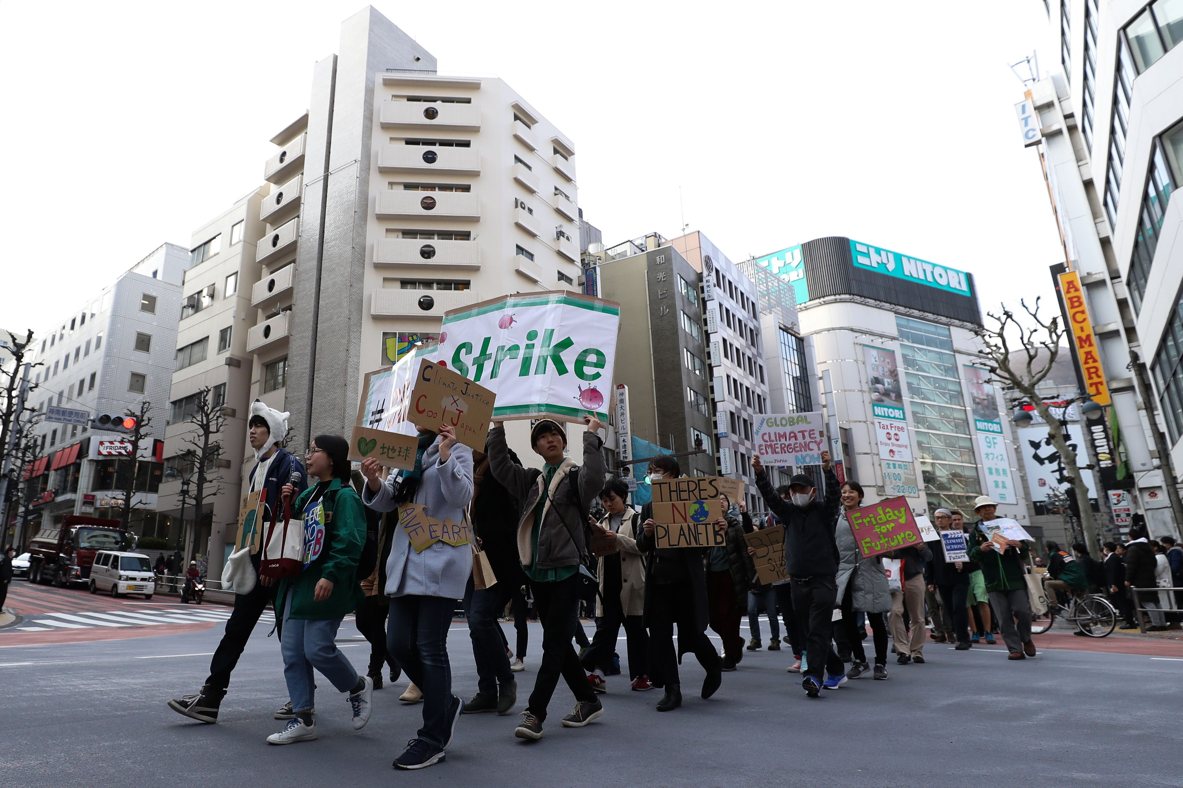 A line of students and protestors cross the street in Tokyo, carrying banners and signs overhead. 