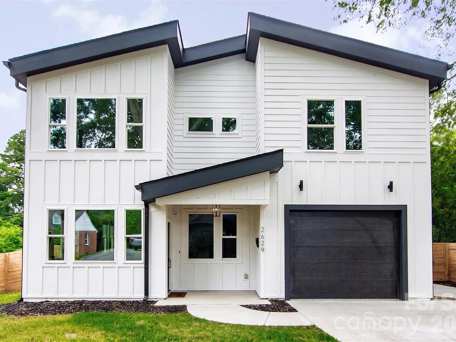 Modern two-story white house with a dark gray roof and black garage door, large front windows on the left, small entry porch at the entrance.