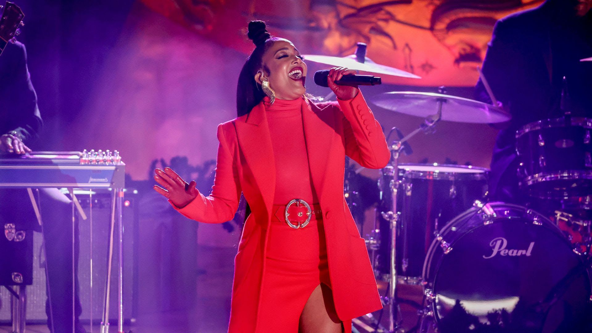 Nashville singer-songwriter Mickey Guyton sings on a purple stage in a red dress.
