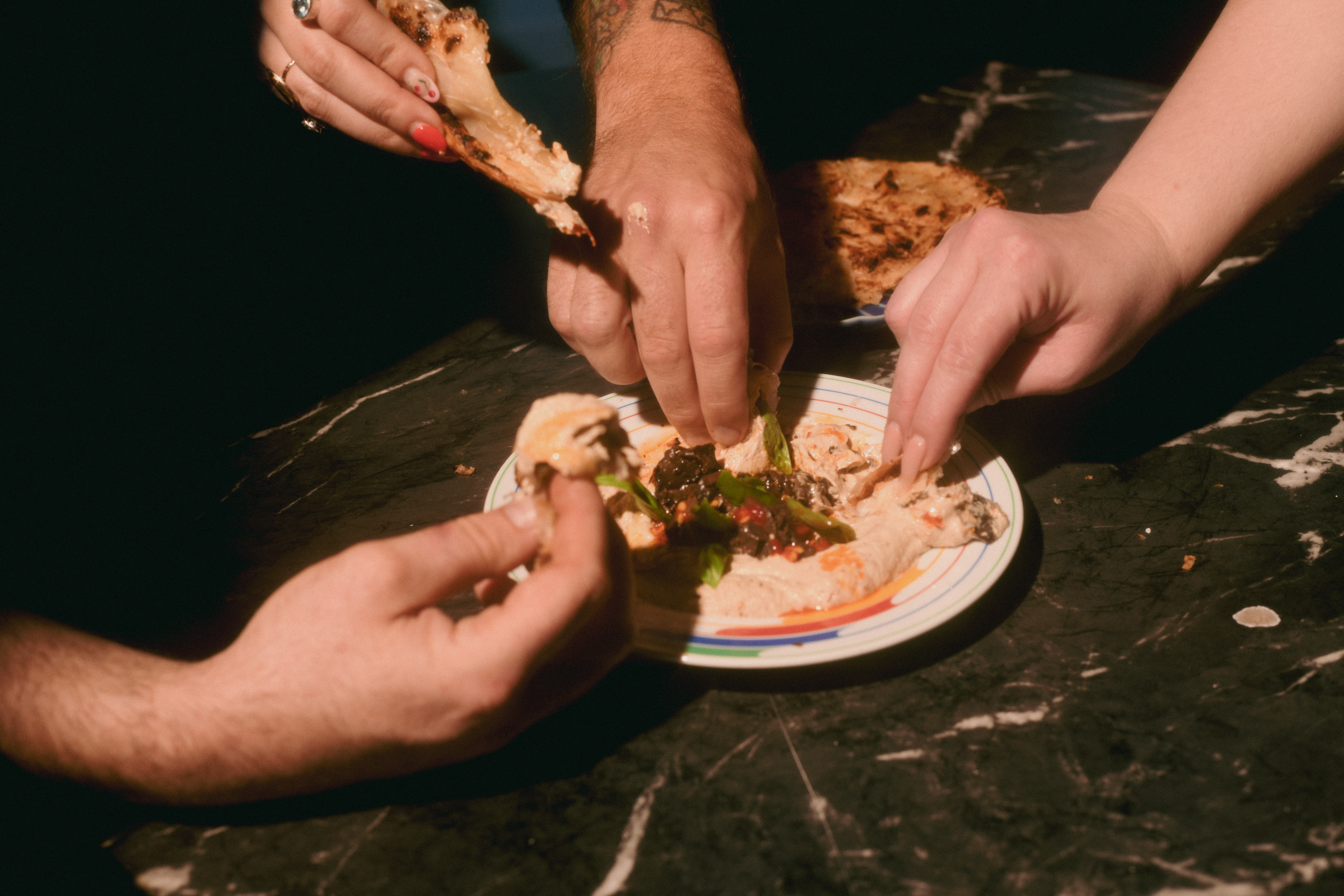 Hands dip bread into a plate of eggplant dip.