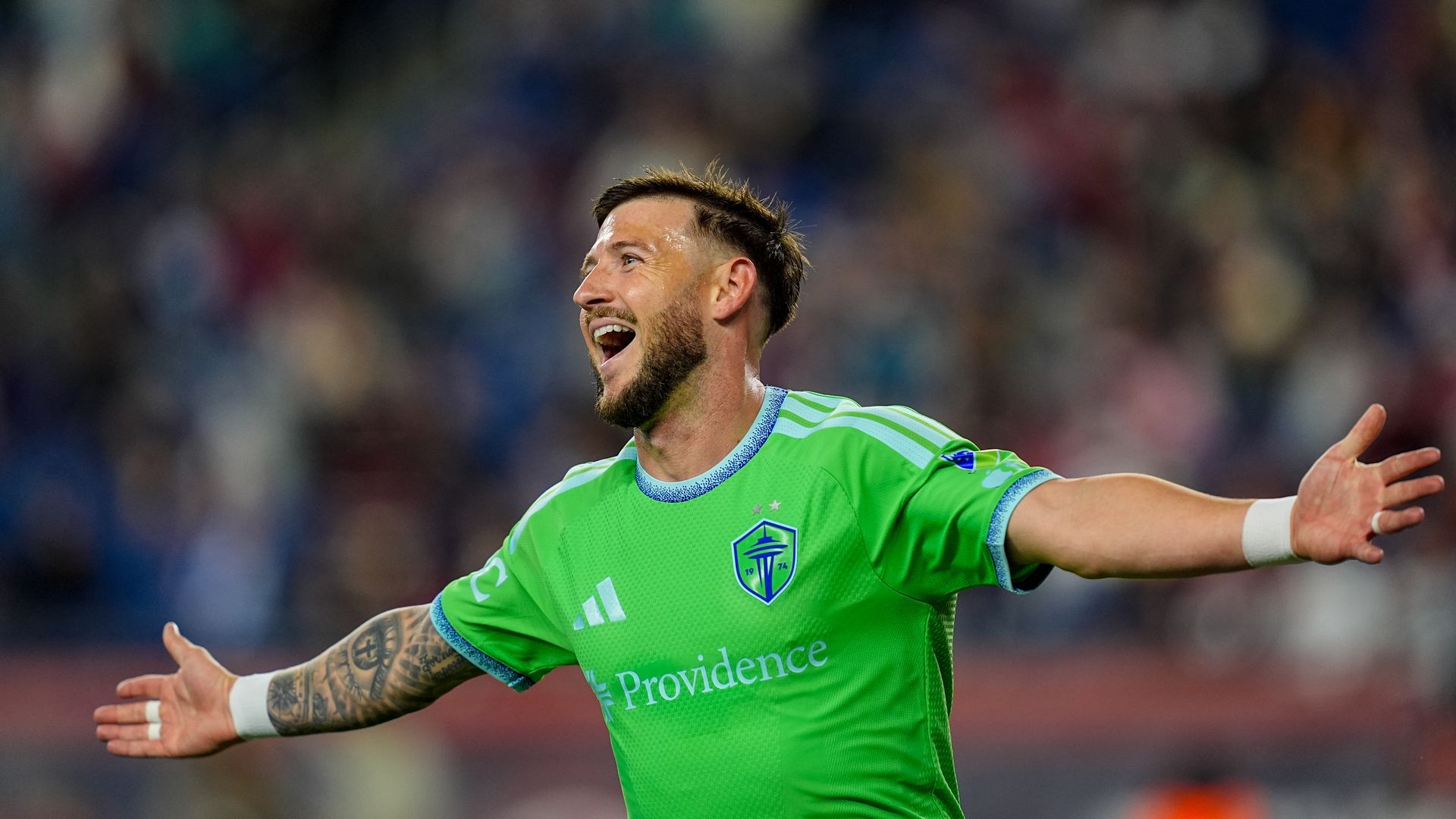 Seattle Sounders midfielder Paul Arriola in green celebrates with his arms outstretched after scoring.