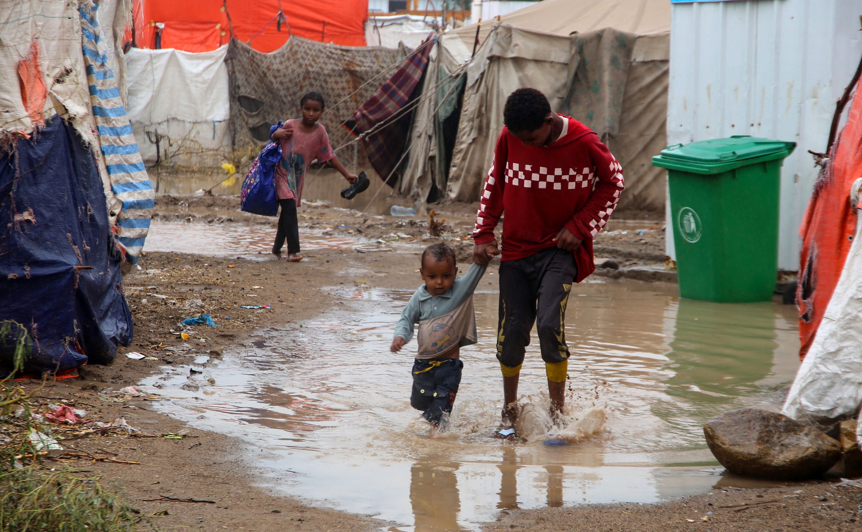 Des enfants marchent dans les eaux de crue devant des tentes endommagées par des pluies torrentielles, dans un camp pour personnes déplacées dans le district de Khokha, dans la province occidentale de Hodeida, ravagée par la guerre au Yémen.