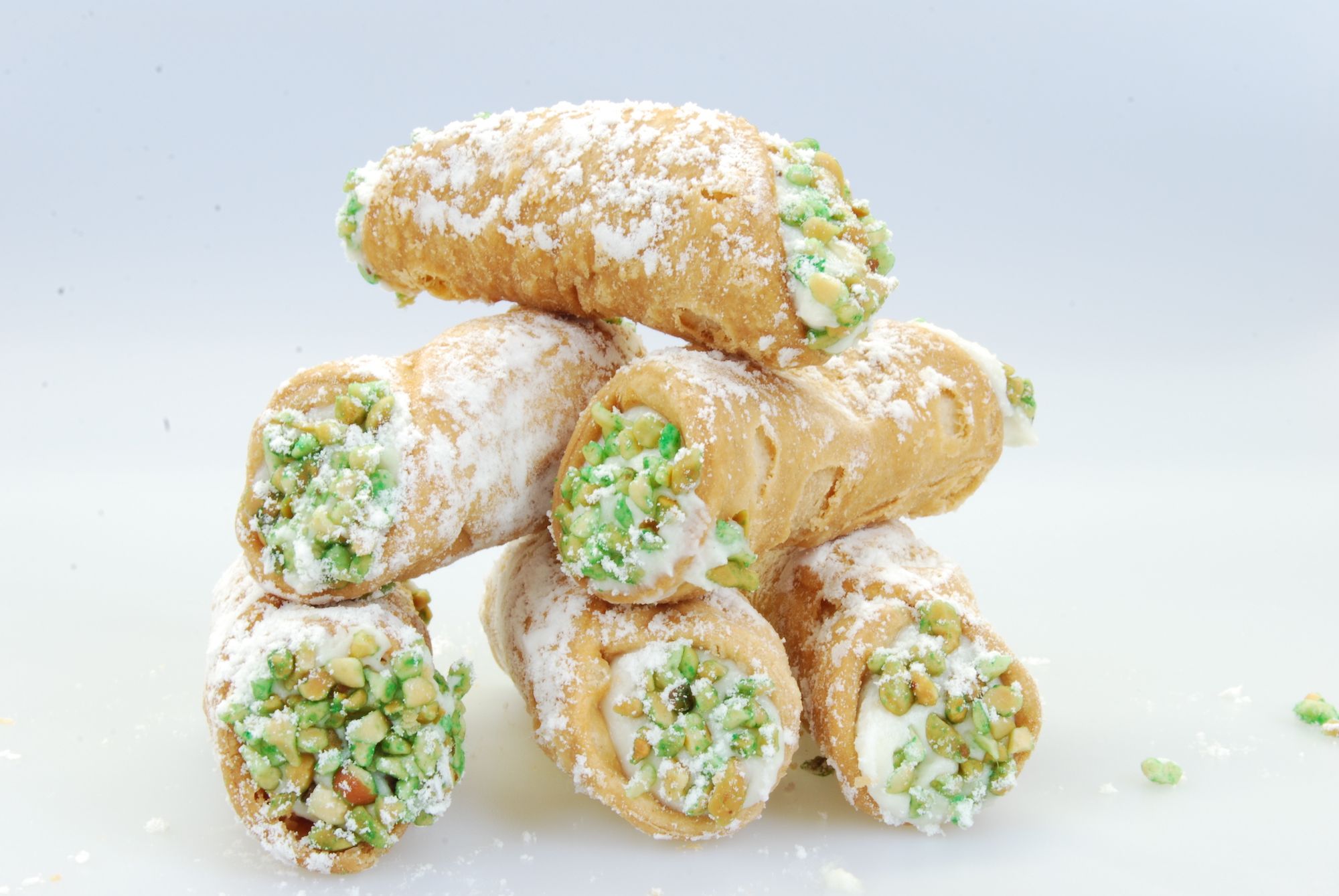 Six cannolis covered in powdered sugar with pistachio and cream filling.