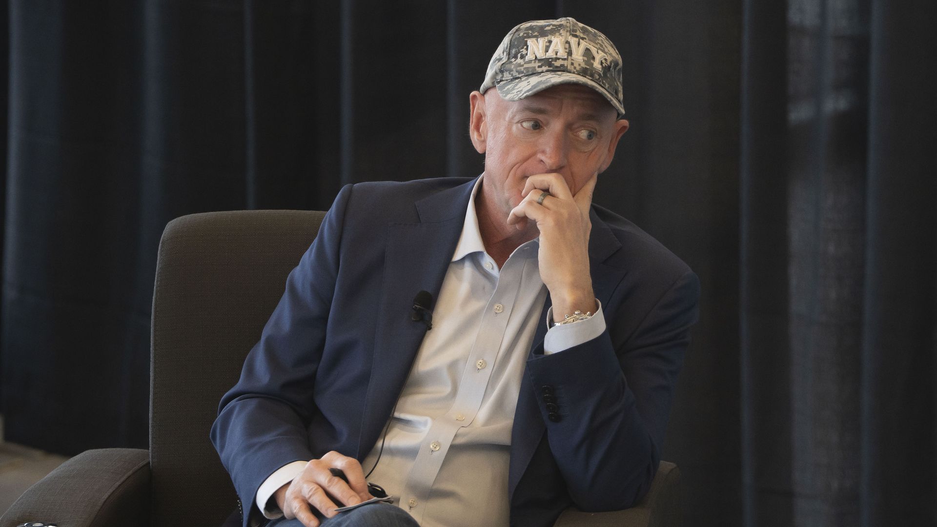 A man sitting in a chair with a hat that says, "NAVY."