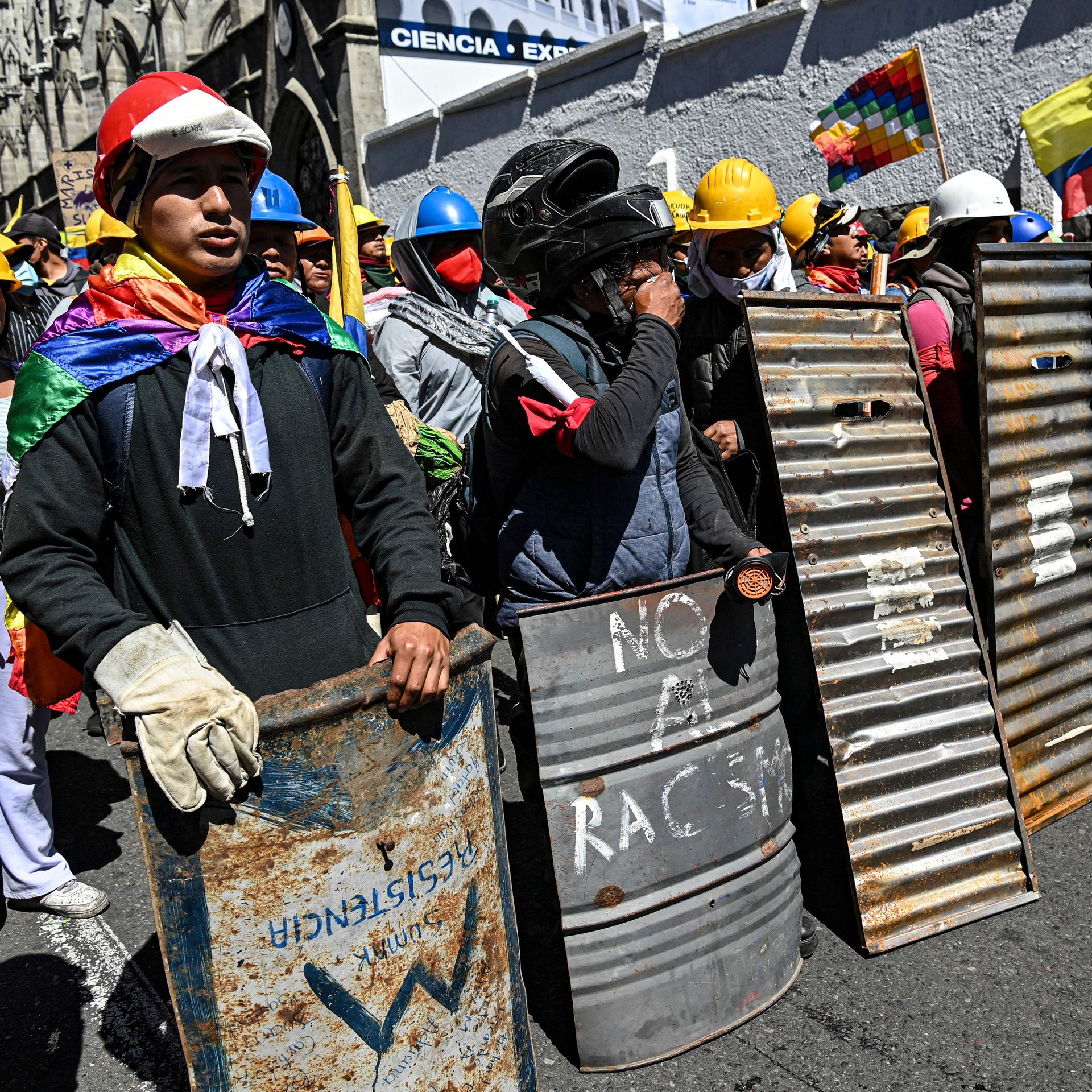 A group of protesters wearing helmets, capes and holding sheets of metal as protection walk through an anti-government protest in Ecuador