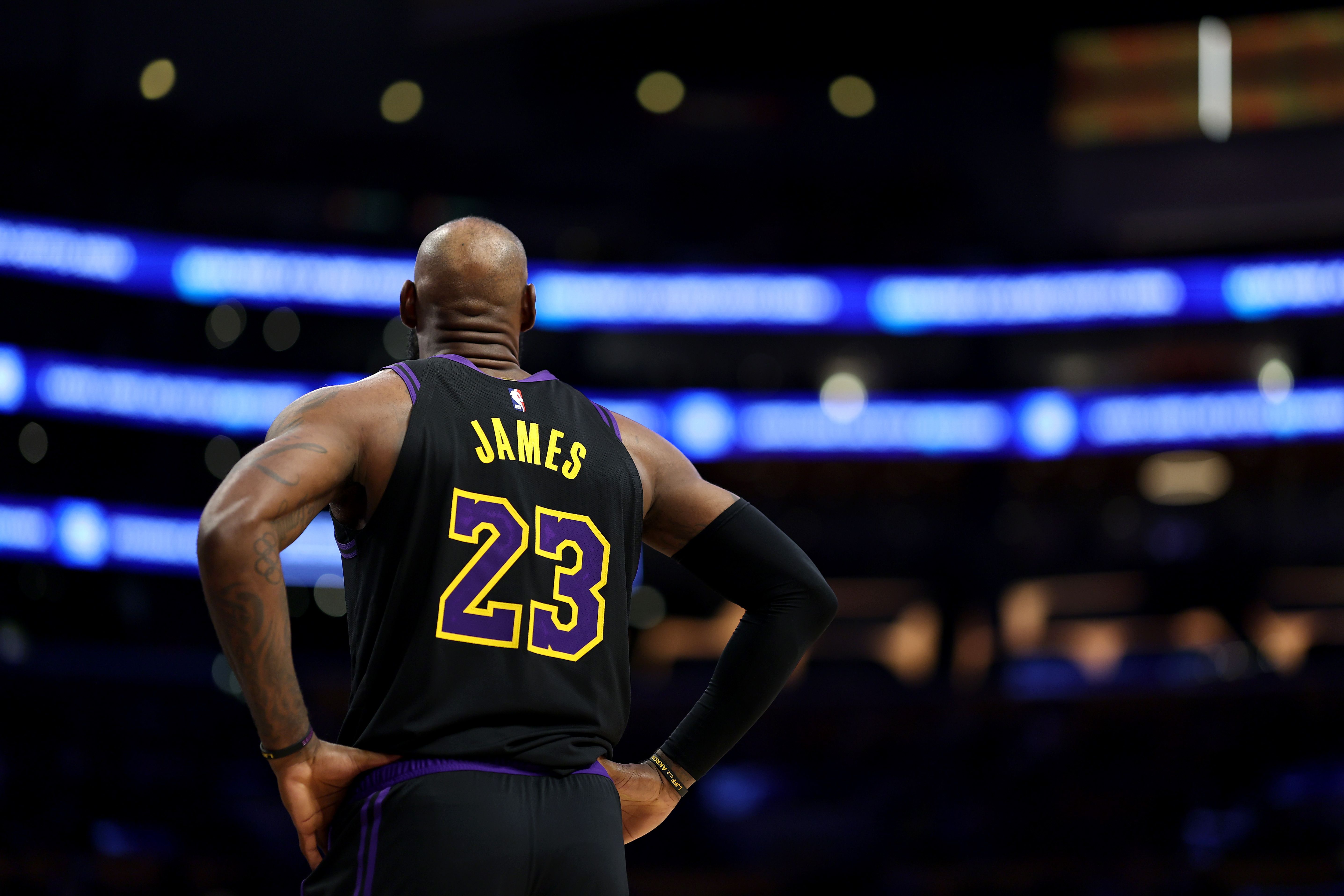 LeBron James, photographed from behind, puts his hands on his hips in black jersey #23.