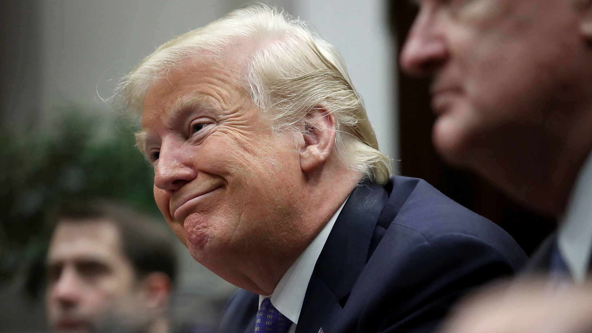 Donald Trump smiles slyly as he leans over a table