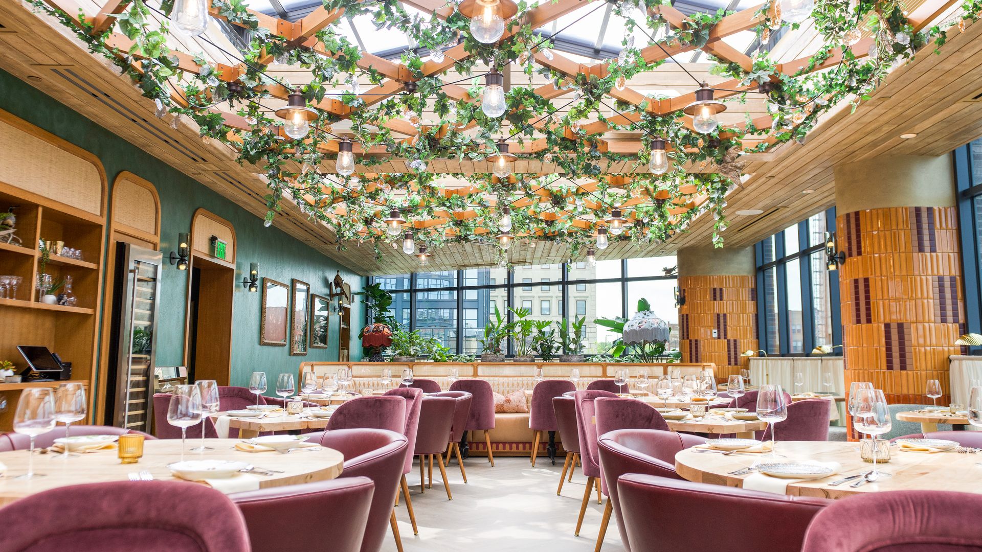 The inside of a fancy restaurant with plants on the ceiling and glass windows.