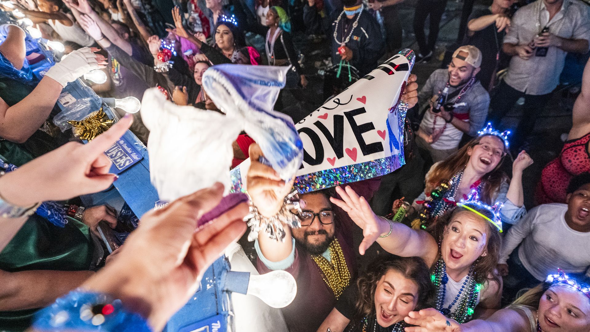 A photo shot from the perspective of a Muses float rider, a hand tosses a shoe toward the parade crowd below.