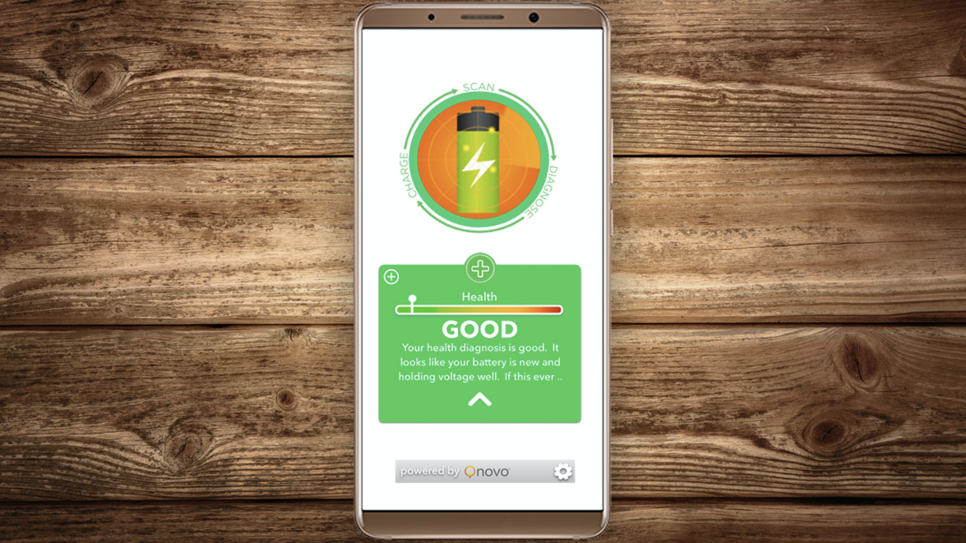 In this image, a cell phone lays on a wooden table and displays a green battery symbol with a "Good" health rating.