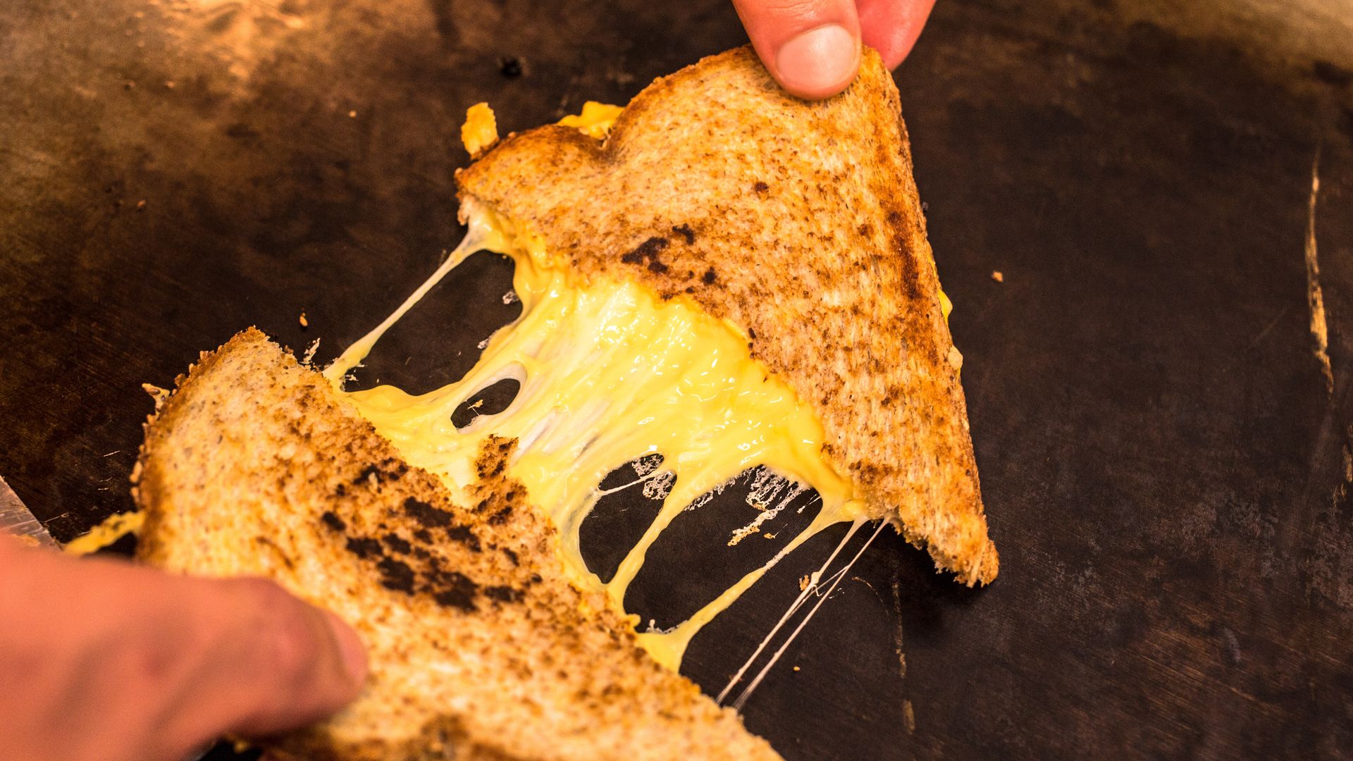 Hands pulling apart a grilled cheese sandwich