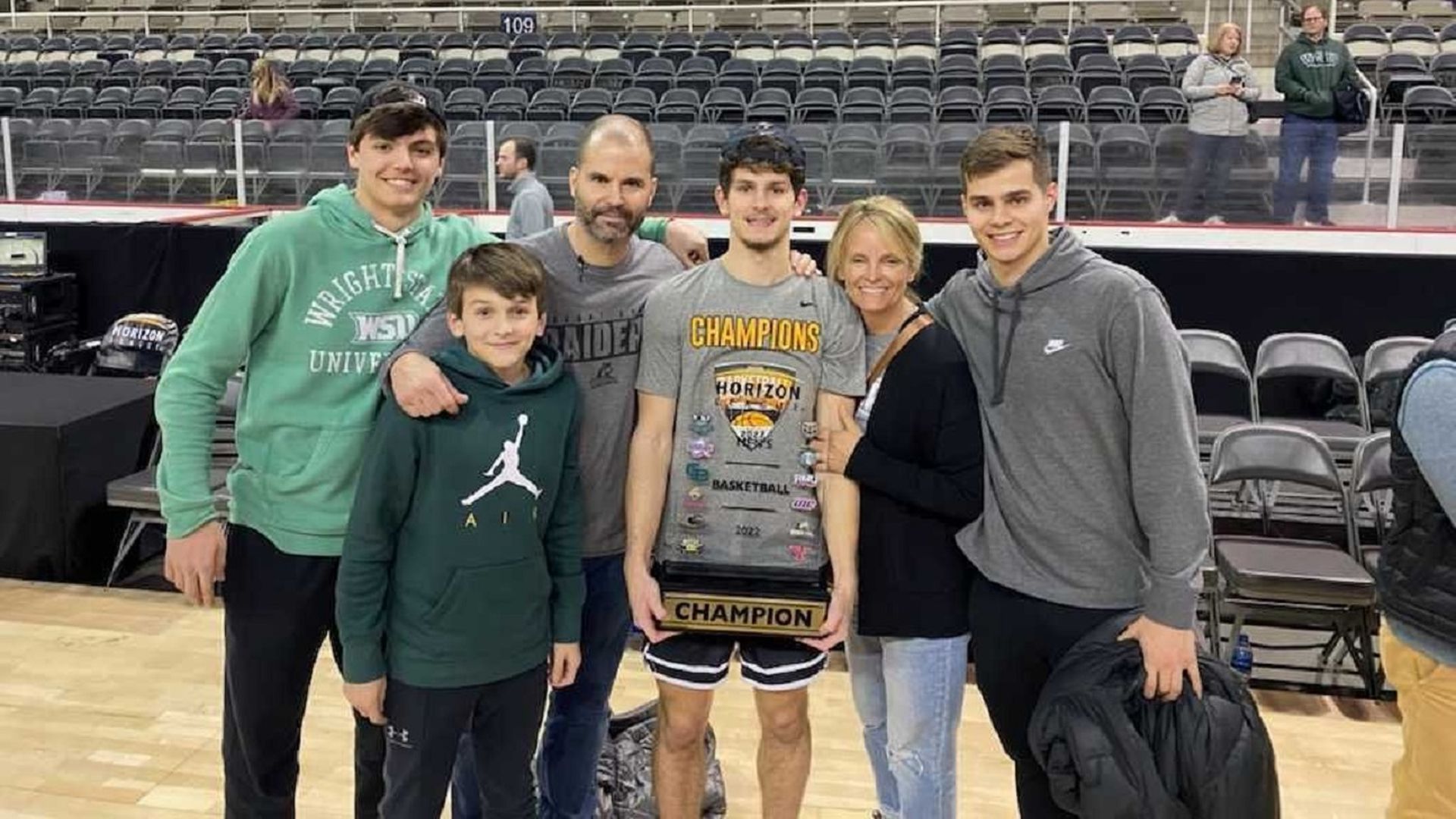 A family poses with a basketball playing son carrying a Horizon League championship trophy.