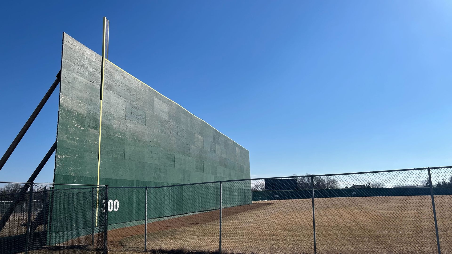 The 37-foot-tall outfield wall at a baseball stadium with a chain link fence and grass in the foreground