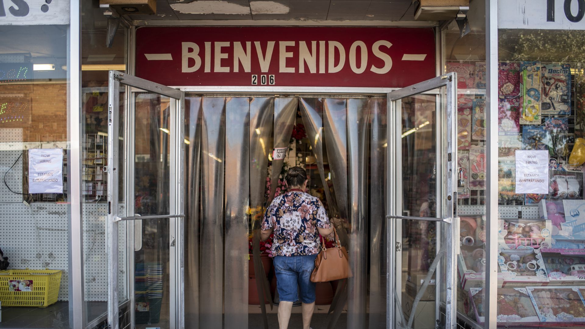 a woman walks into a store with a large sign above it that says "bienvenidos"