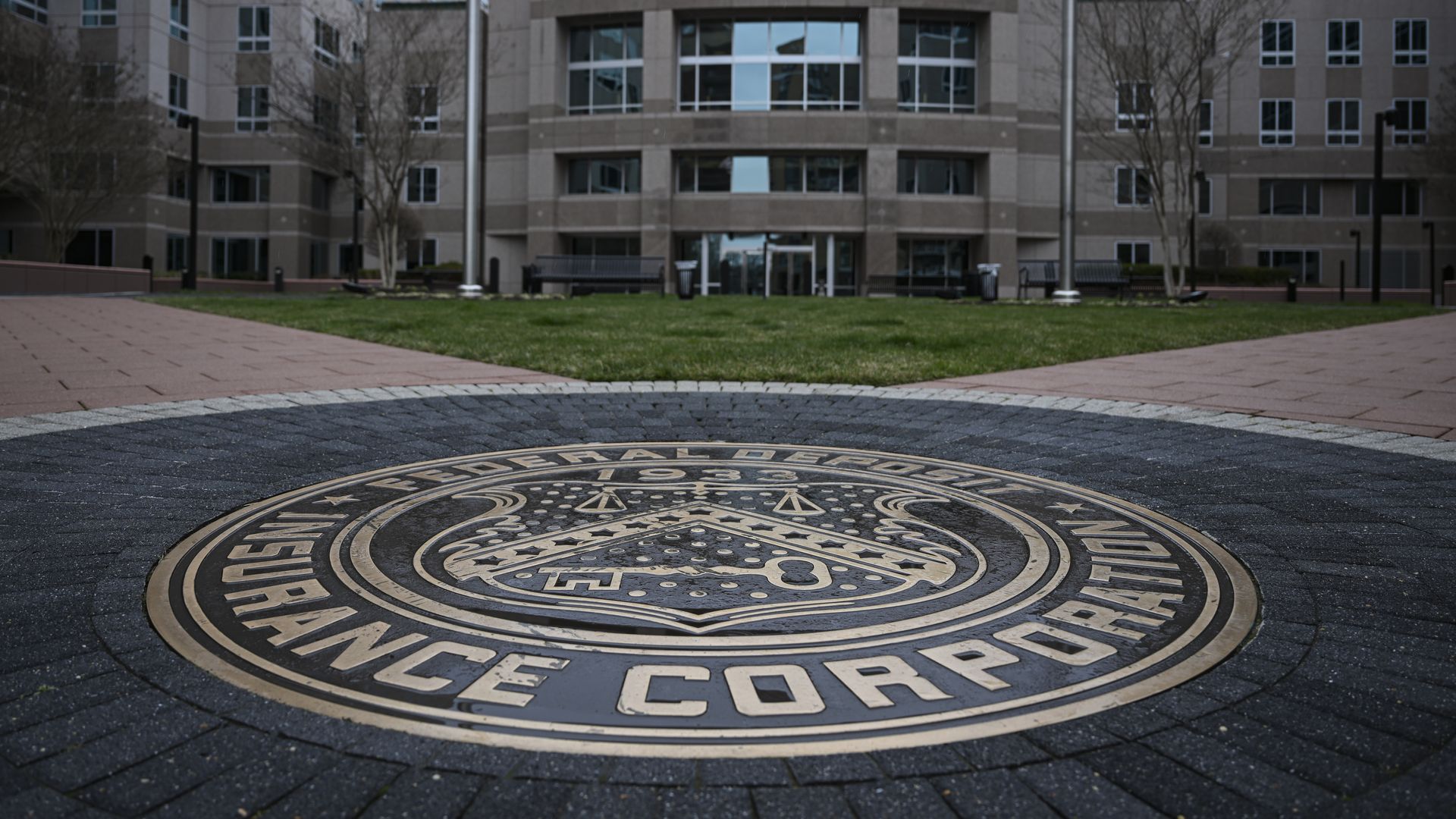 A large round government logo on the ground in front of a stately building