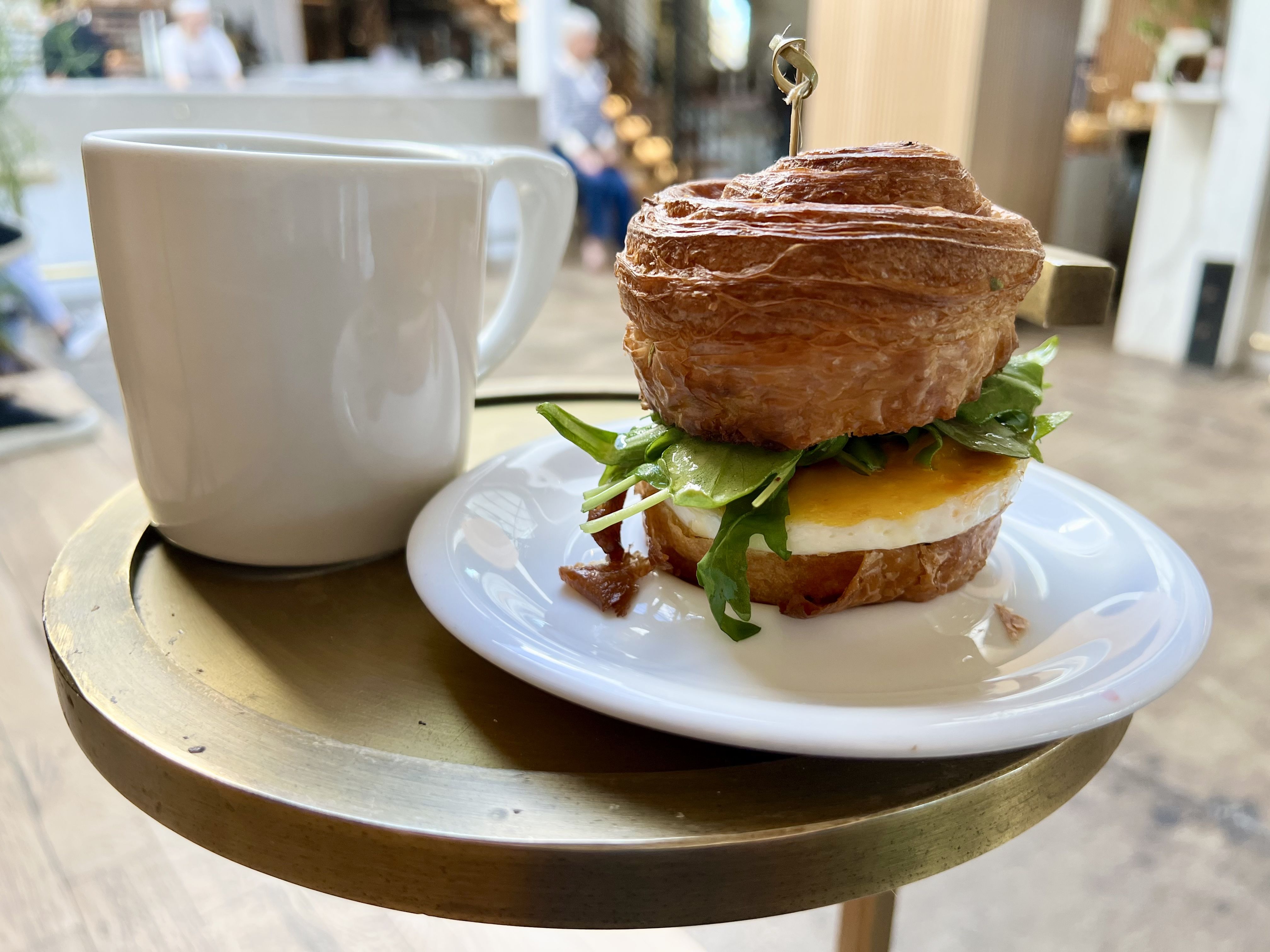 bacon egg and cheese on a croissant, next to a cup of coffee