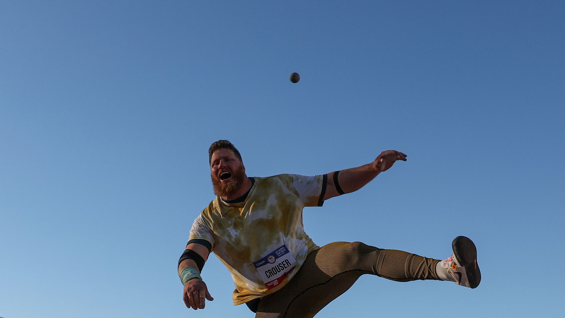 Shot putter with shot in the blue sky behind him