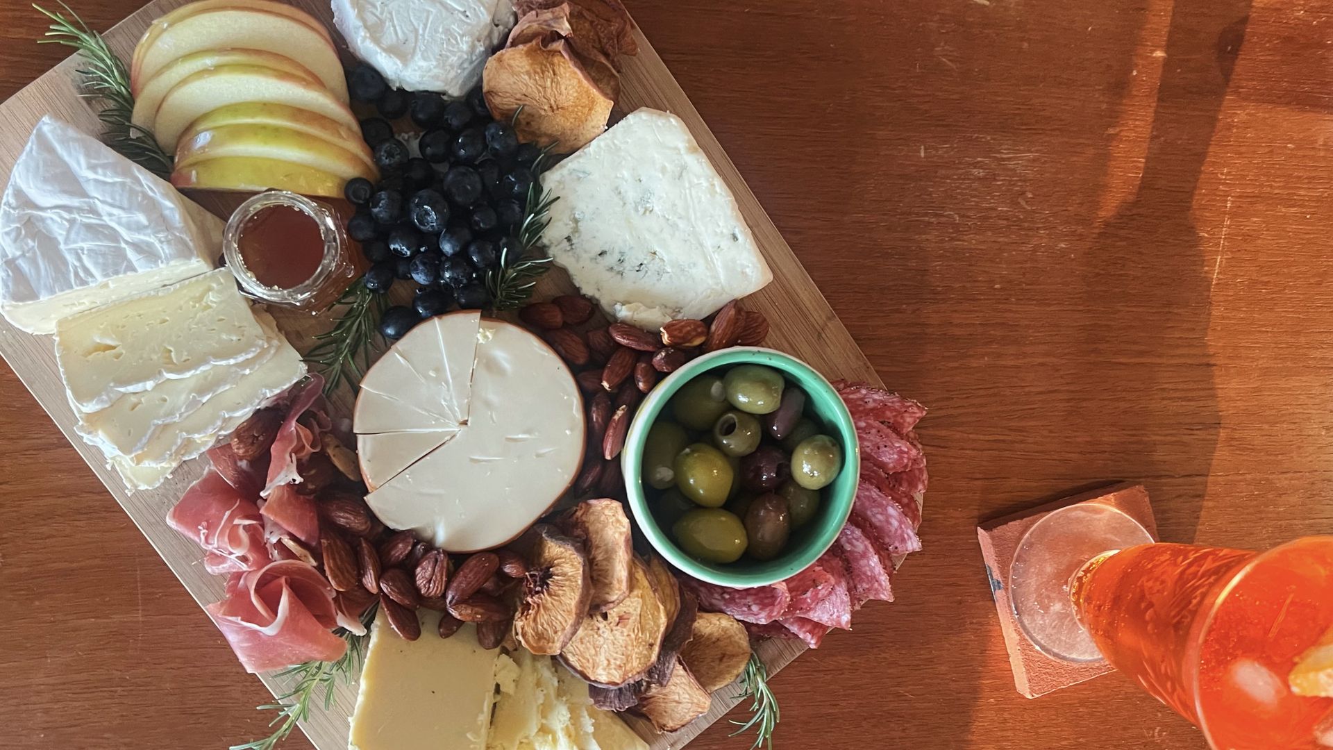 A photo of a cheese board on a table filled with cheese, meats, olives, apples and other fruit.