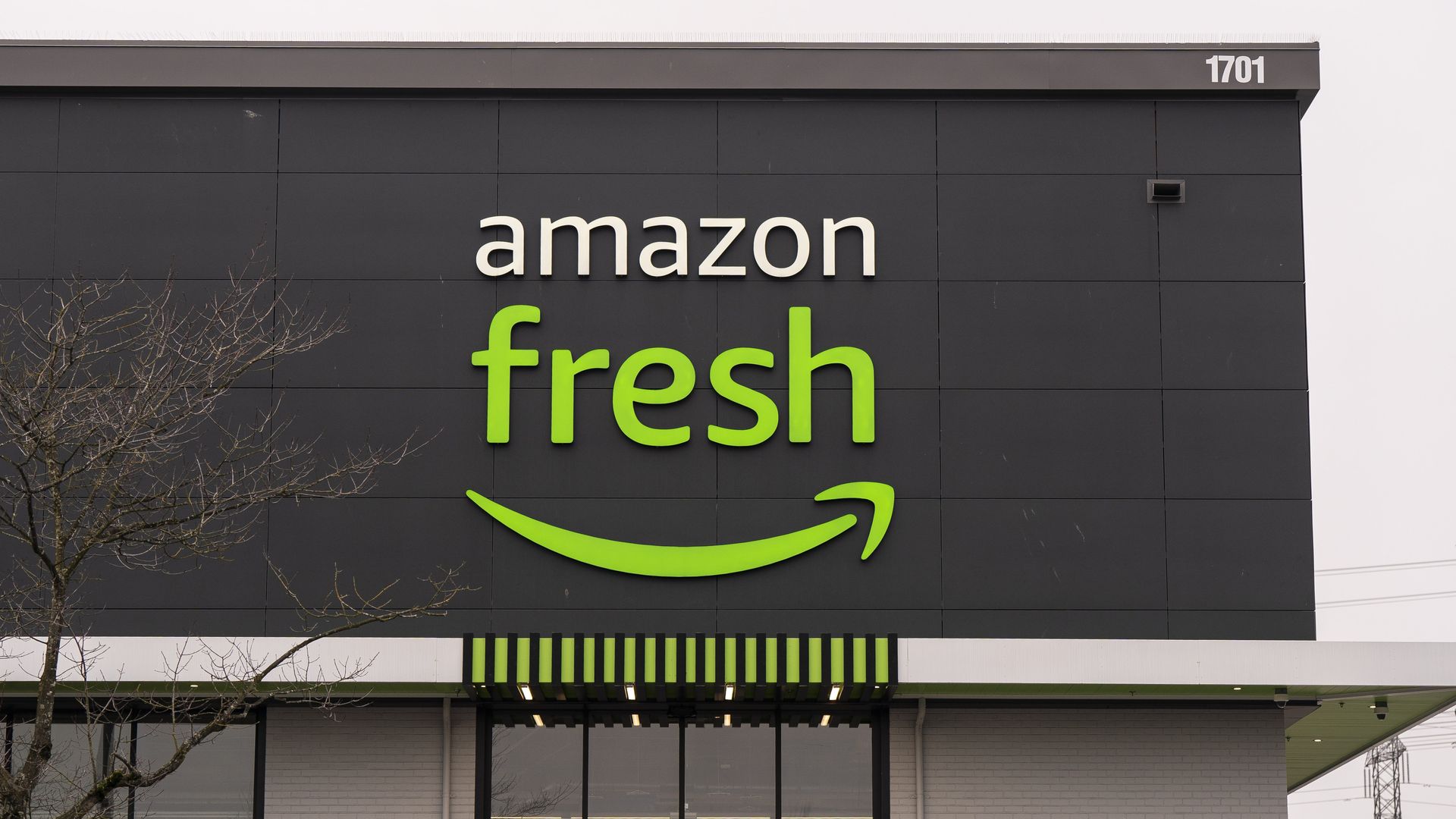 Exterior of an Amazon Fresh store with a black and gray facade, green and white logo, and store address number 1701 on top right corner.